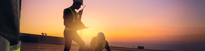 A photo of a roofing professional speaking into a walkie-talkie with a sunset in the background