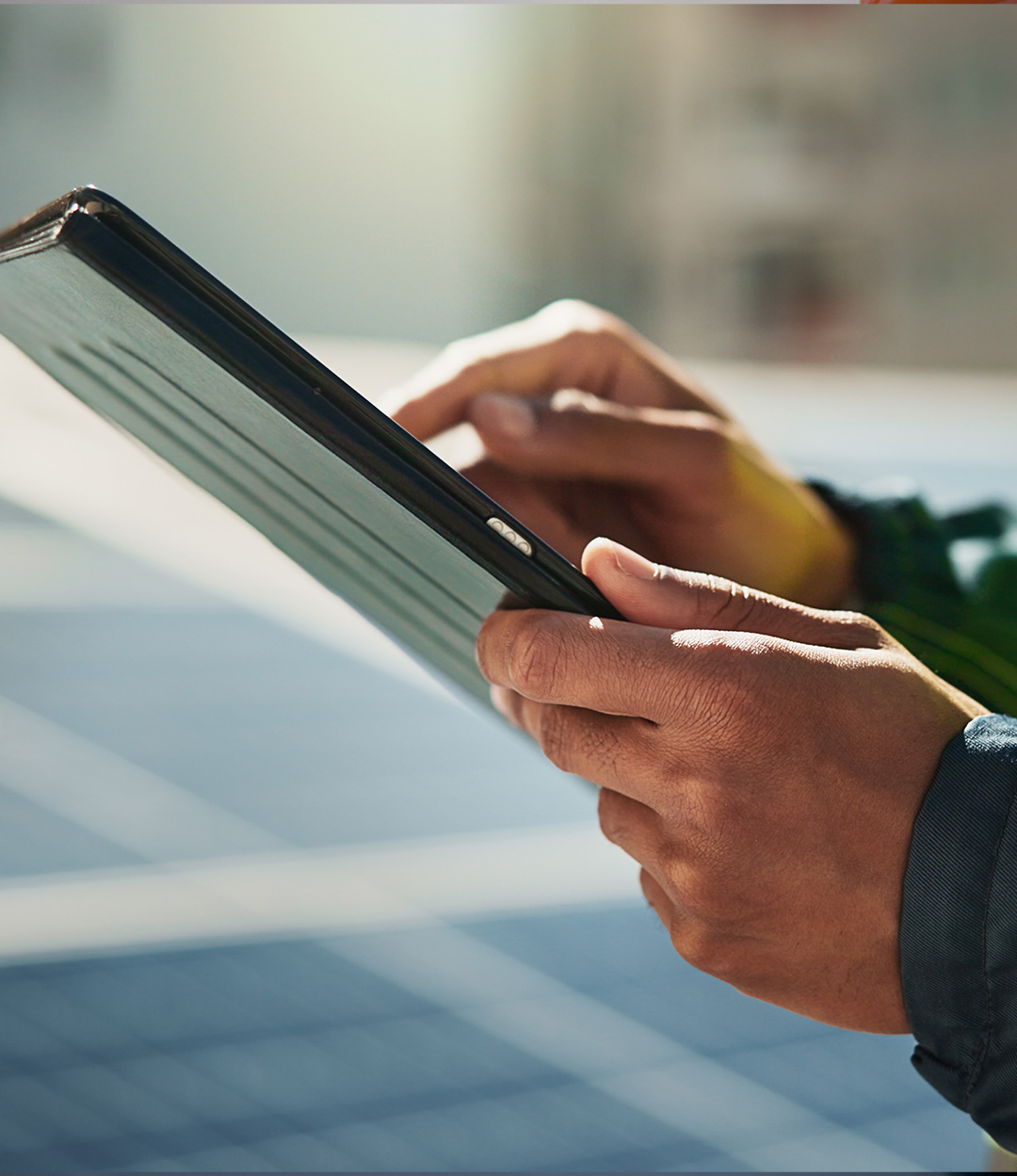 Person holding and using a tablet device outdoors in sunlight.