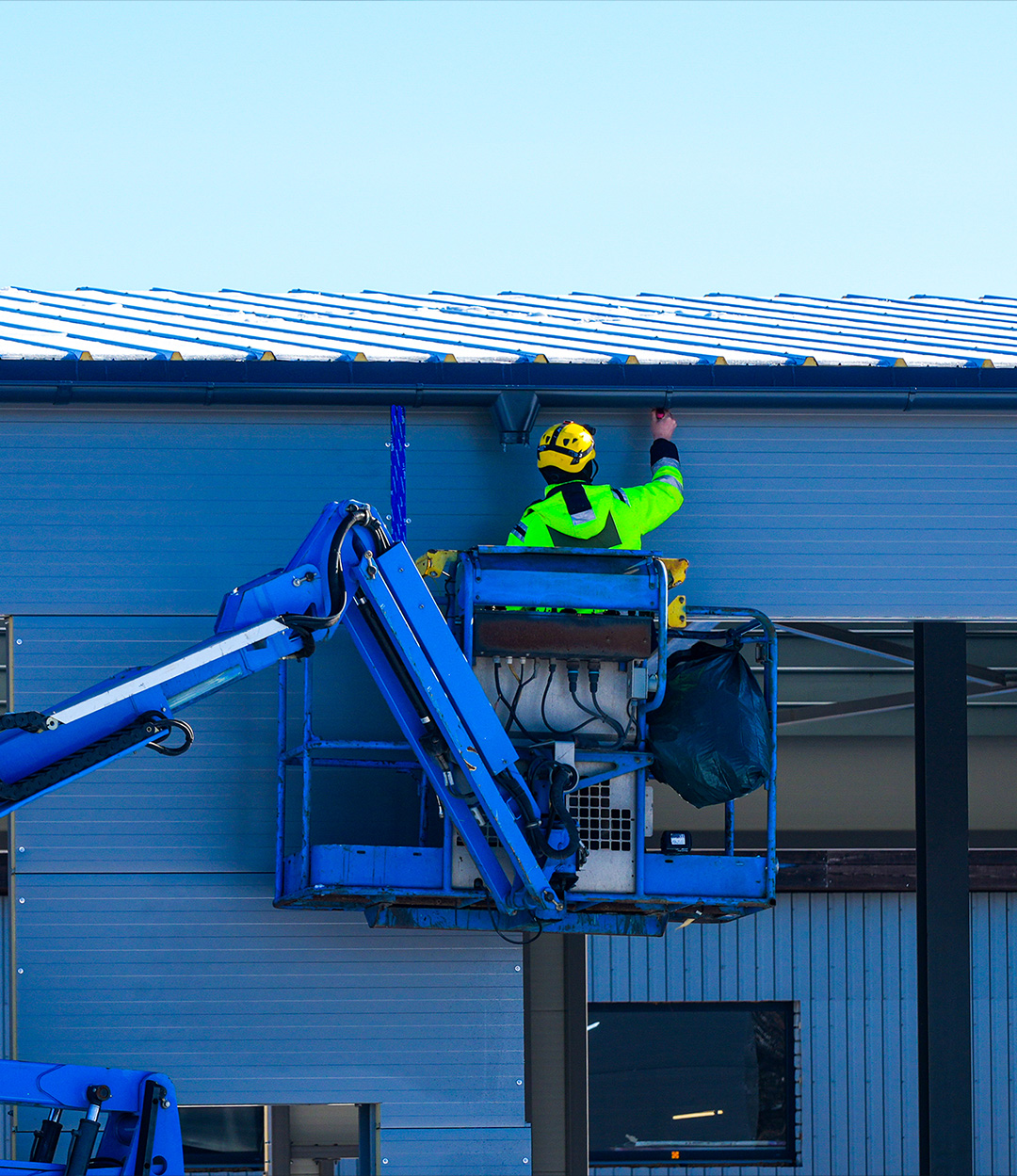 Inspecting a blue metal clad commercial roof using a scissor lift