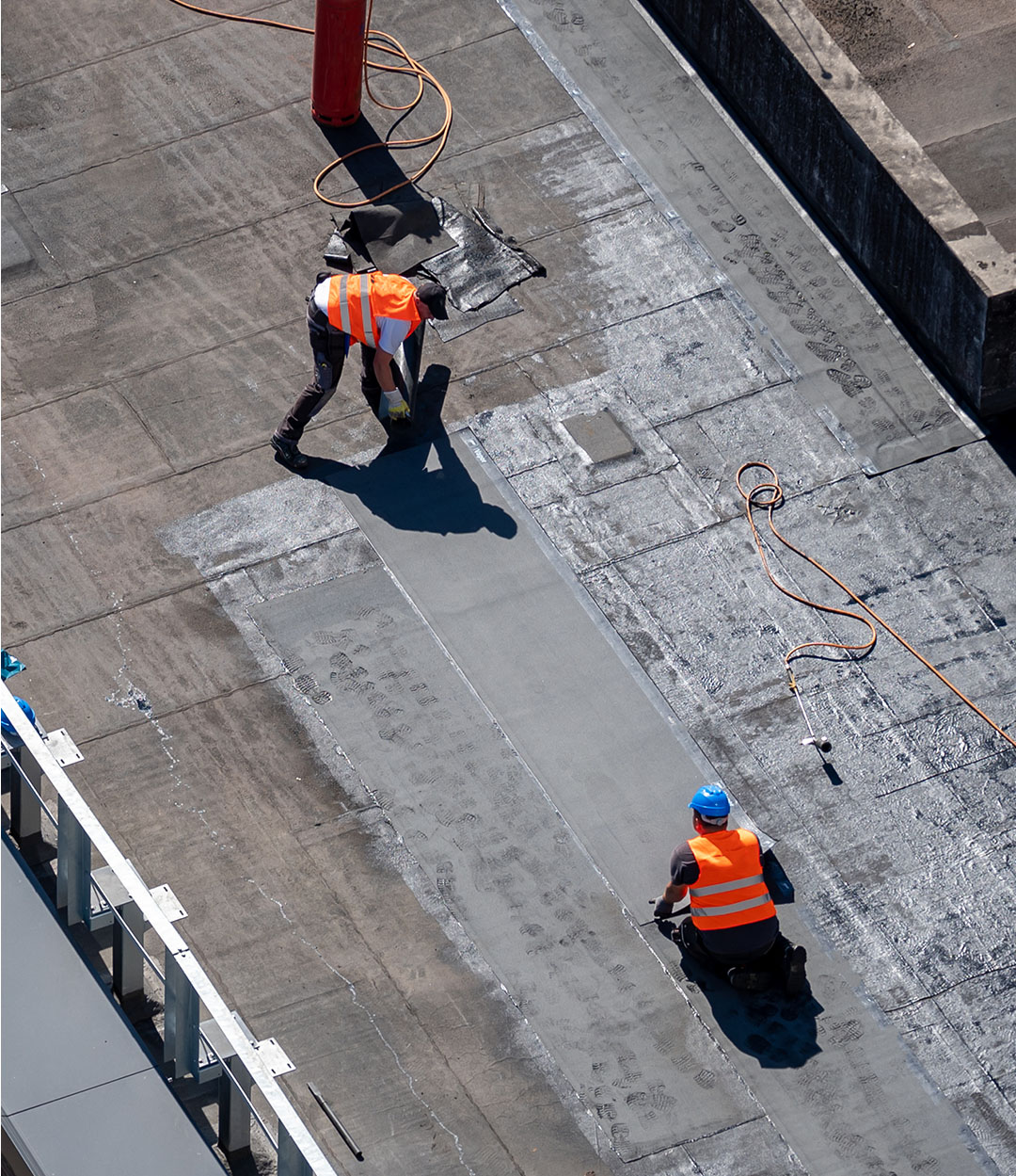 Roofing professionals putting down tar paper on a large commercial rooftop.