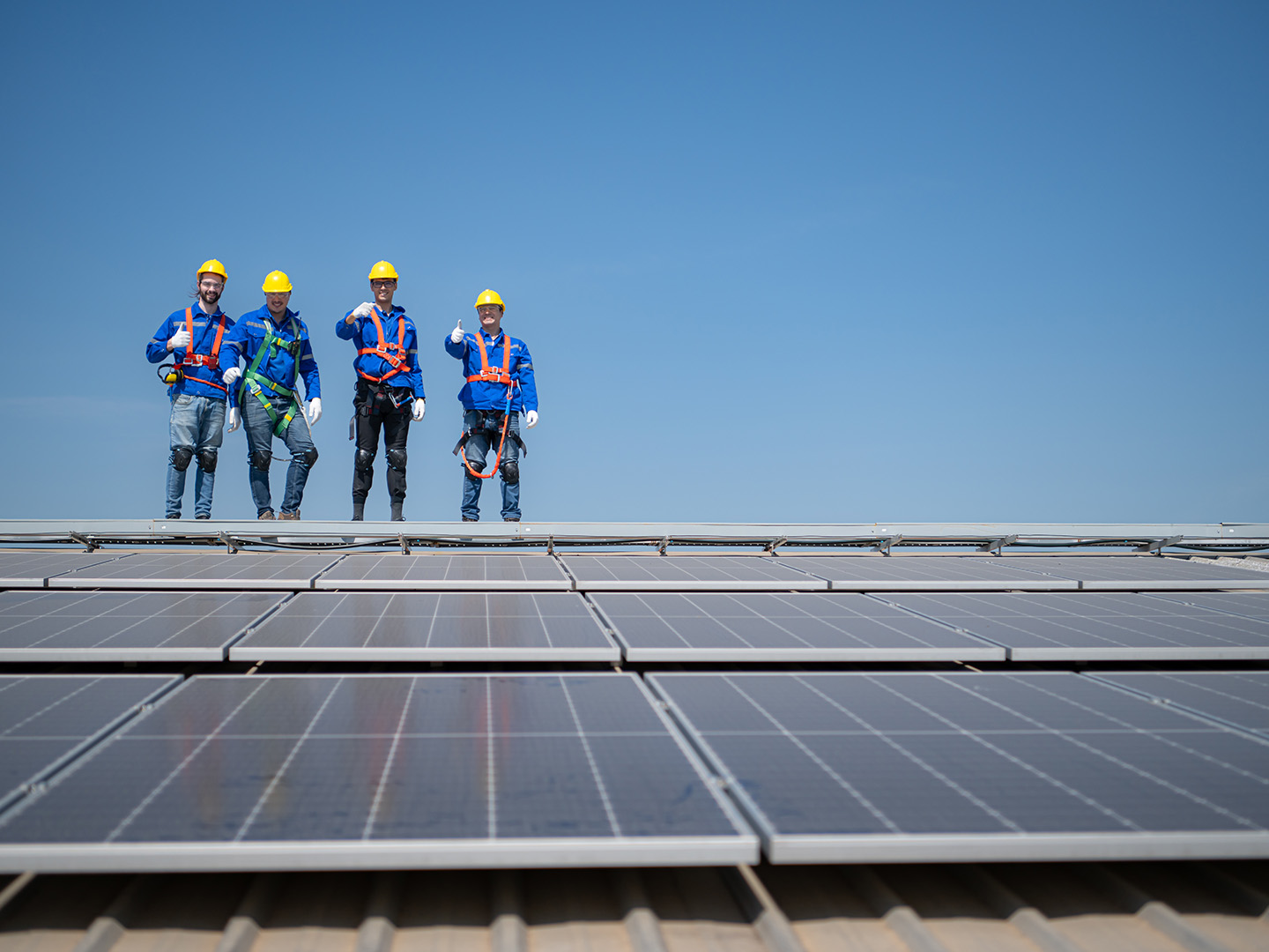 4 roofing professionals standing side by each on a new commercial roof covered in solar panels.