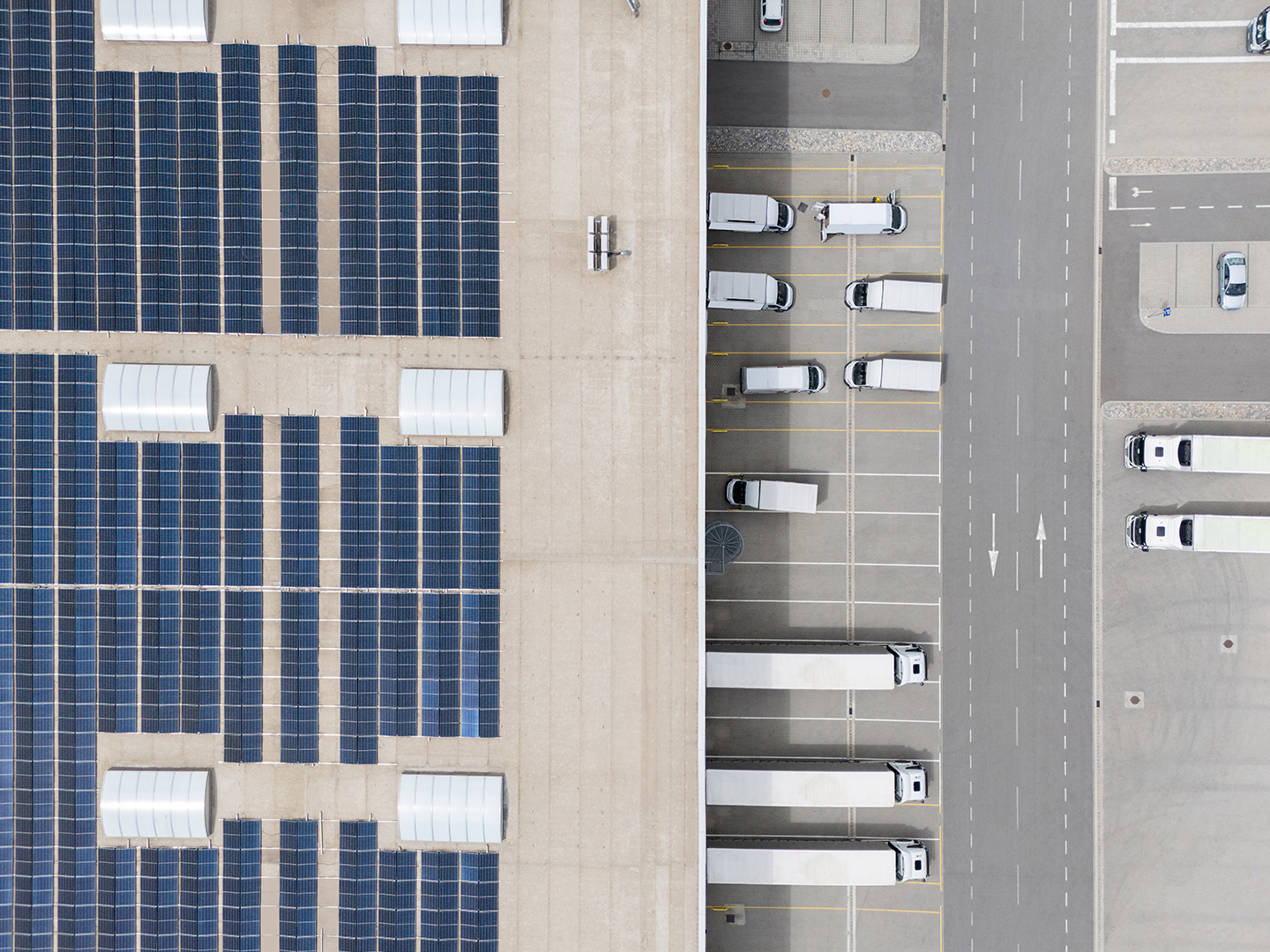 Aerial view of solar panels on roof left and trucks parked in loading dock area right.