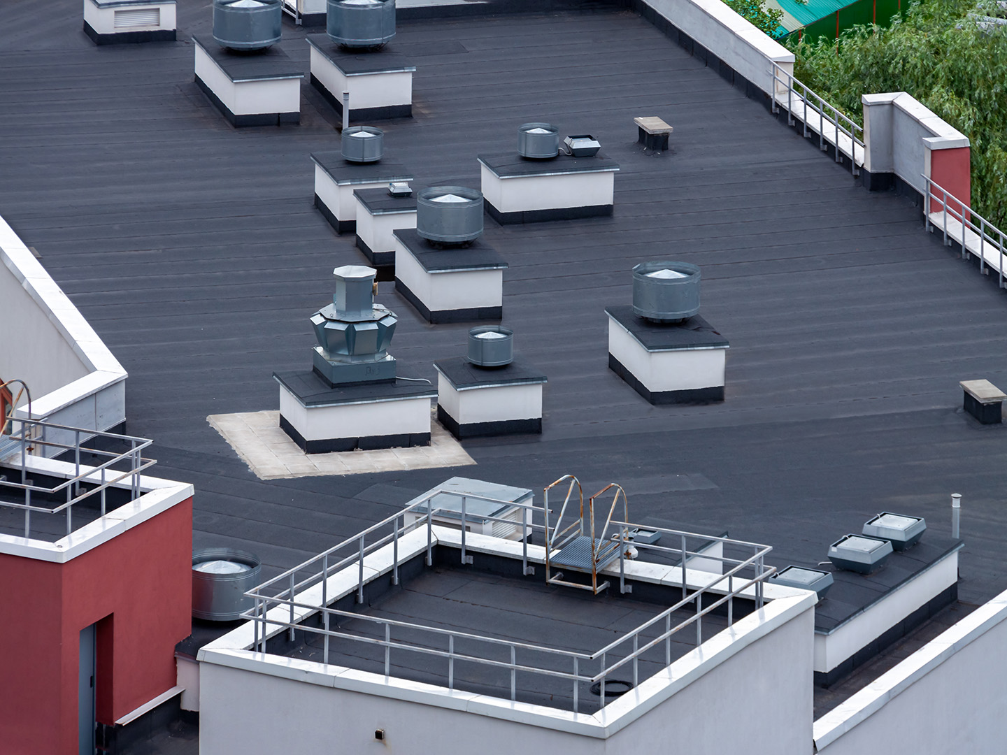 Flat black rooftop with multiple ventilation units, white railings, and a red building wall.