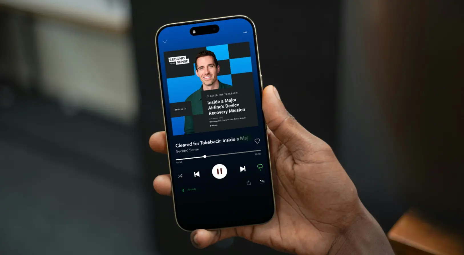 Hand holding a smartphone displaying a podcast episode titled 'Inside a Major Airline's Device Recovery Mission' on the Second Sense podcast app.