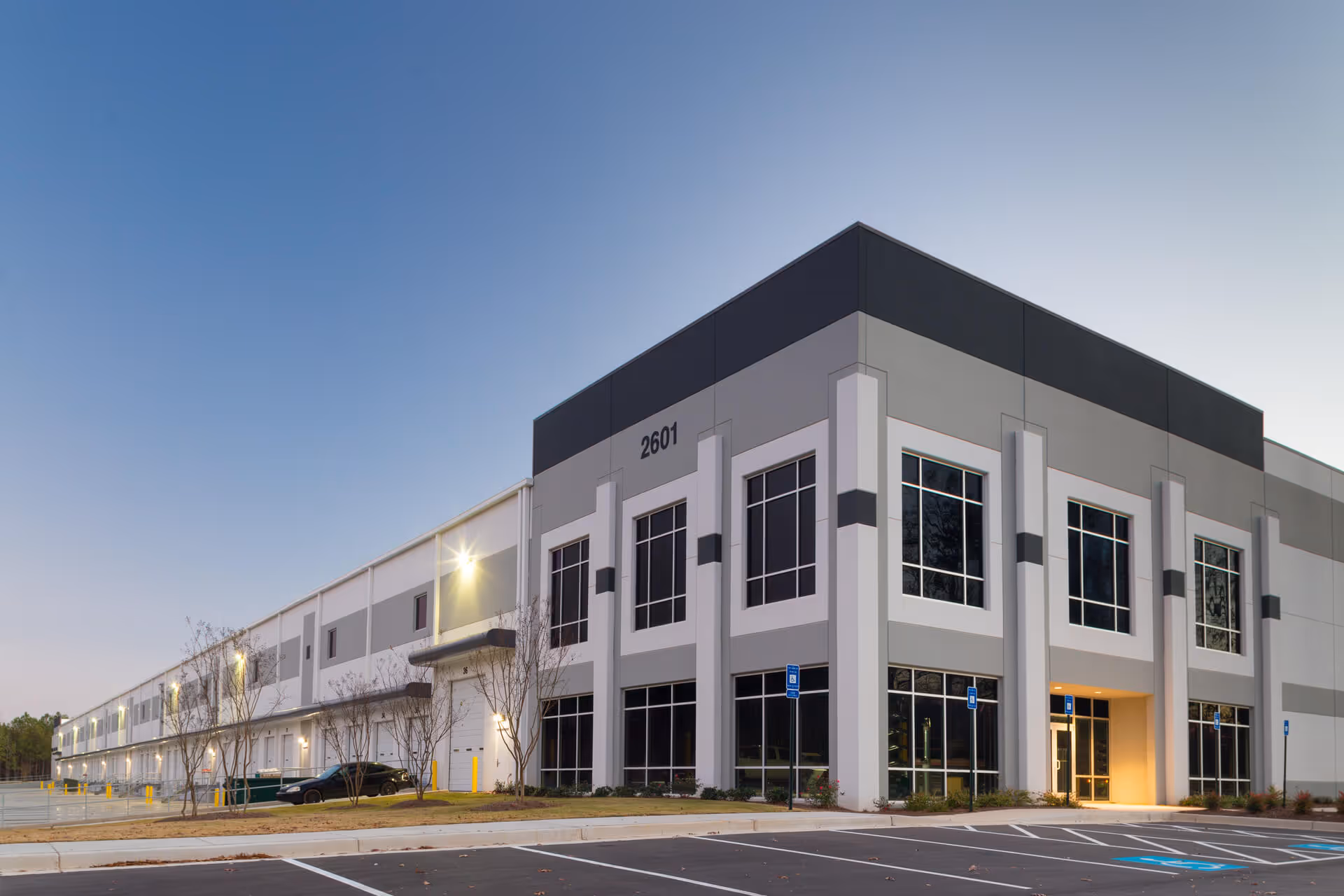 Modern large industrial distribution center building with multiple windows and loading docks at dusk.