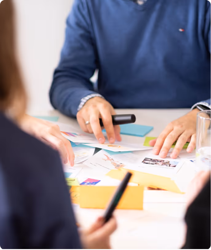 Personen in einem Meeting arrangieren Dokumente und bunte Zettel auf einem Tisch.