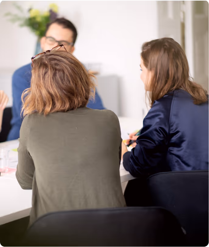 Drei Personen sitzen an einem Tisch und führen ein Gespräch in einem Büro.