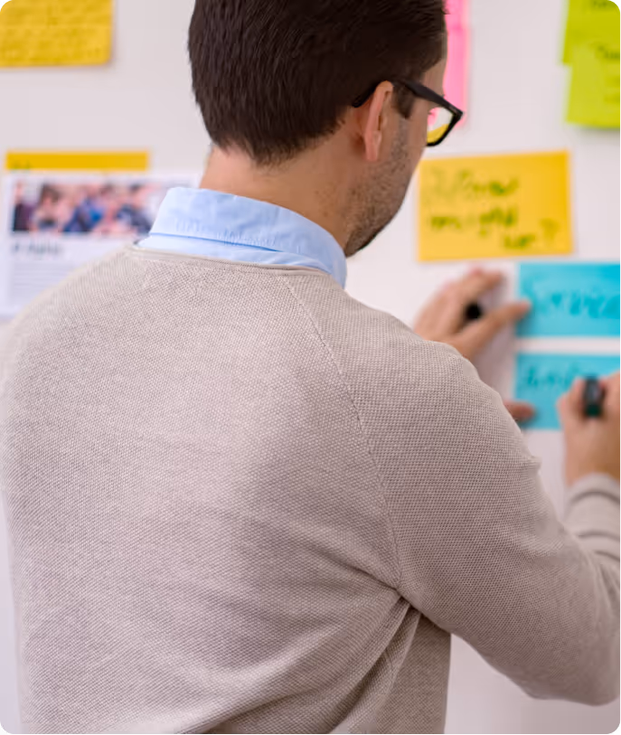 Mann schreibt auf bunte Notizzettel an der Wand während eines Brainstormings.