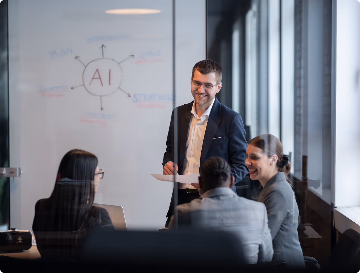 Mann präsentiert AI-Strategie an ein Team im Büro mit Whiteboard und Laptops.