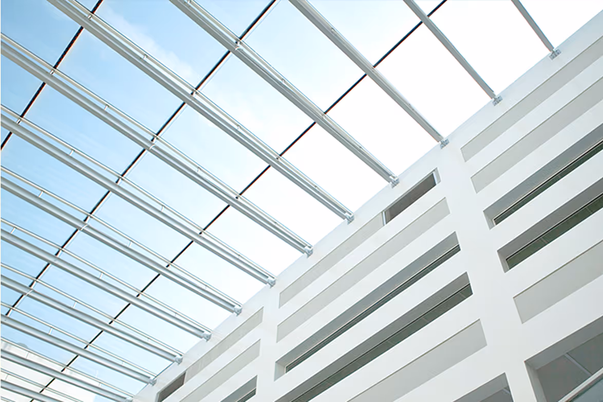 Moderne Glasdachstruktur über einem weißen Gebäude mit rechteckigen Öffnungen.