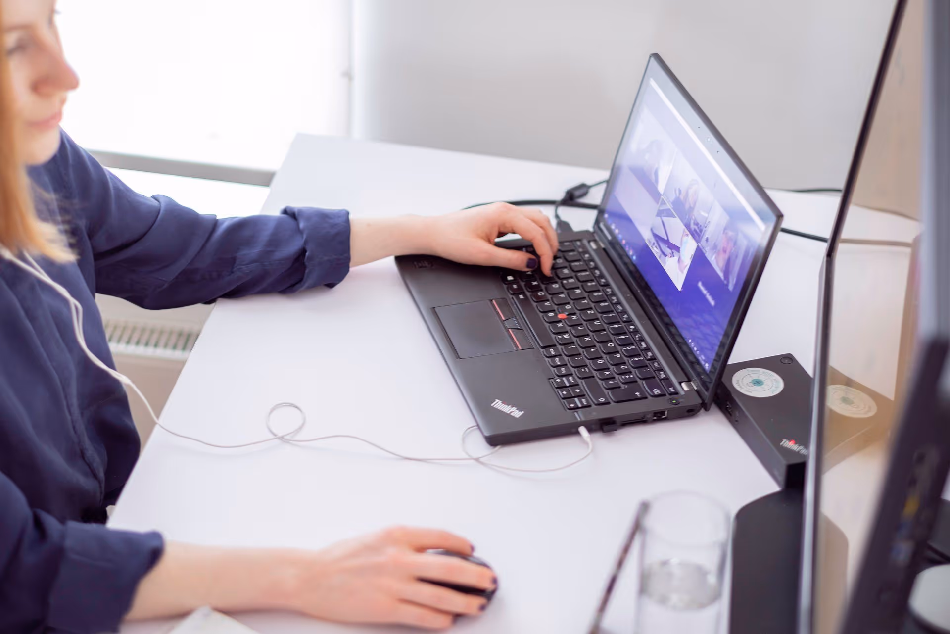 Frau nutzt Laptop für Videokonferenz, eine Hand auf der Tastatur, die andere an der Maus.