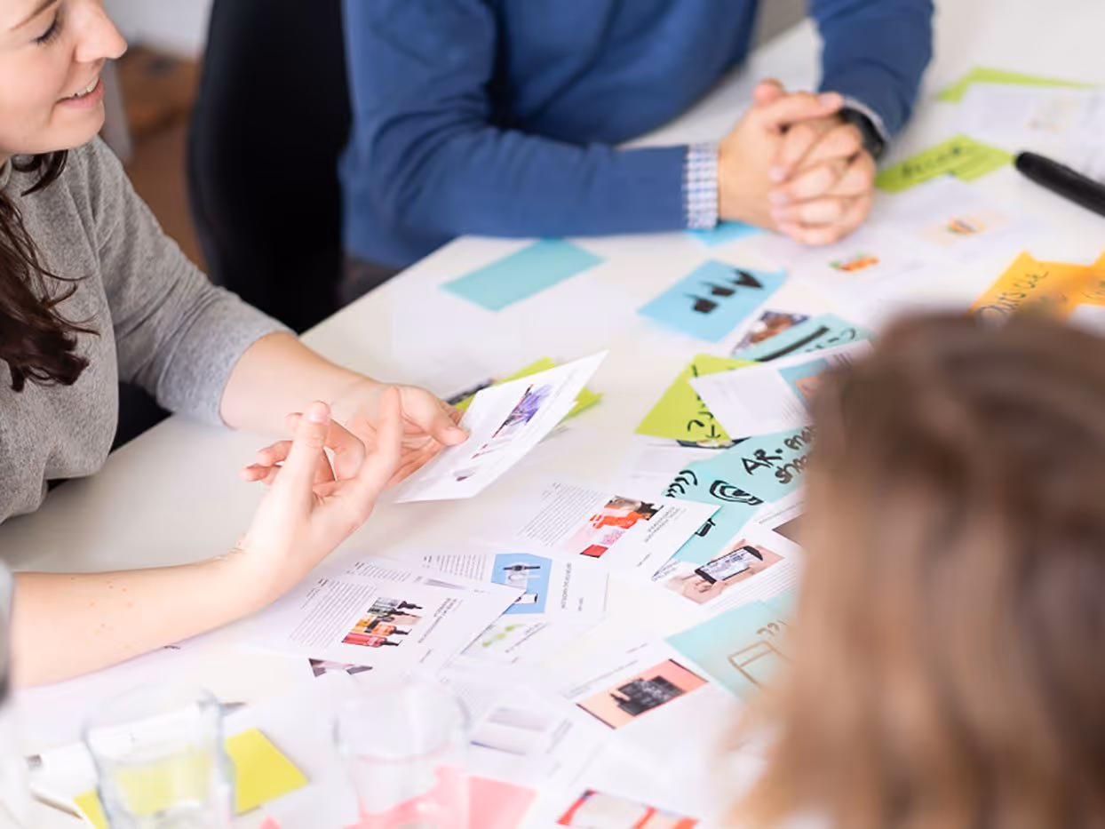 Drei Personen diskutieren über Notizen und bunte Zettel auf einem weißen Tisch.