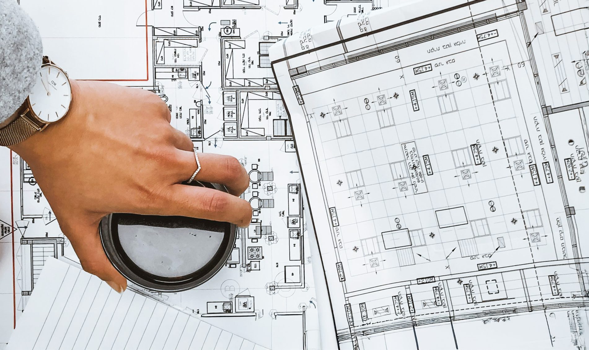 A hand holds a magnifying glass over a technical drawing