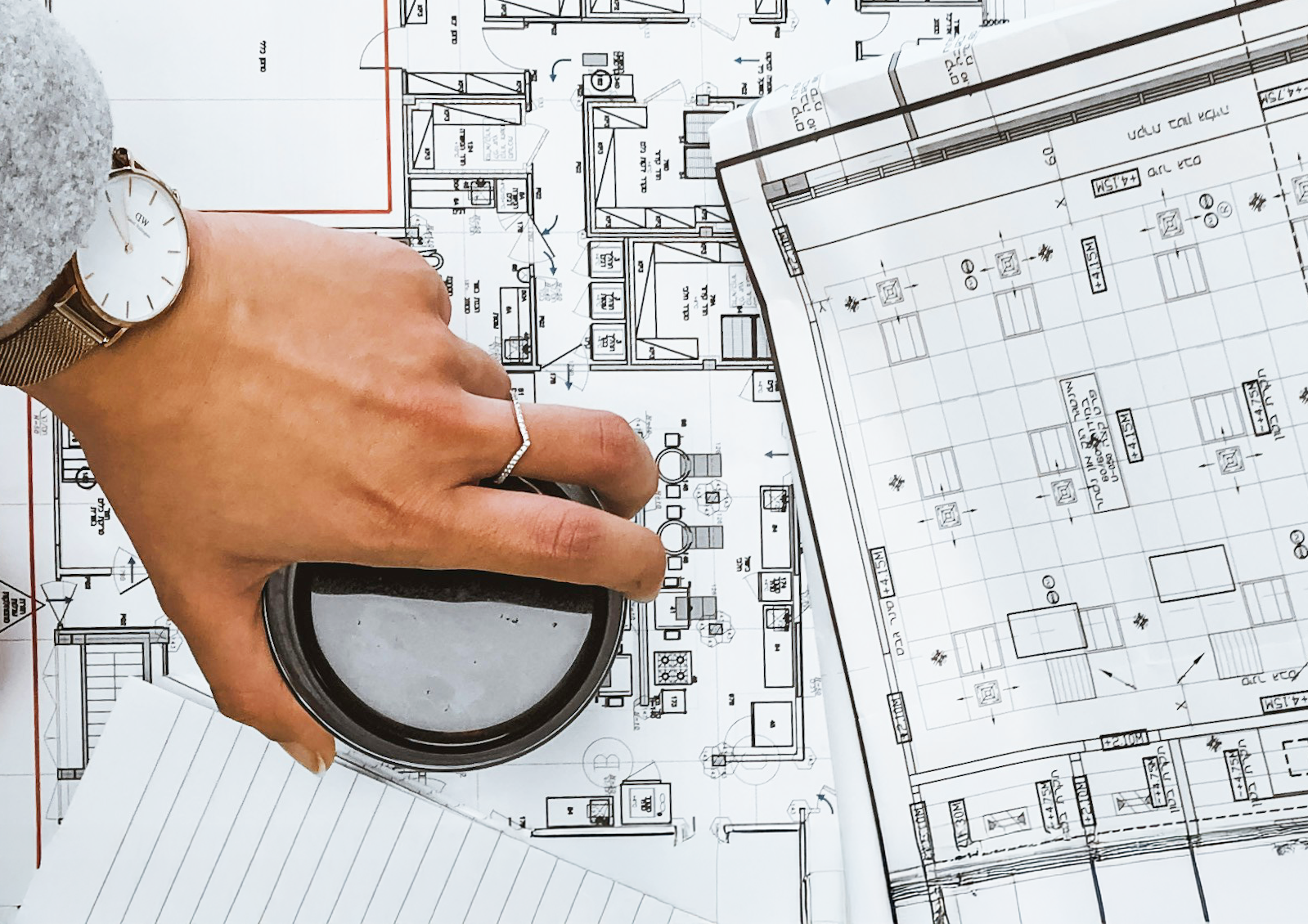 A hand holds a magnifying glass above a technical drawing