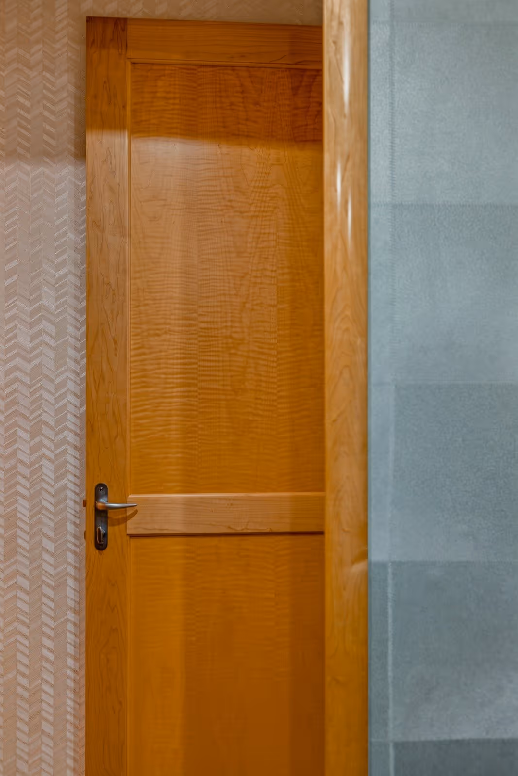 Partially open wooden door with a silver handle, next to a beige patterned wall and a blue-gray textured wall.