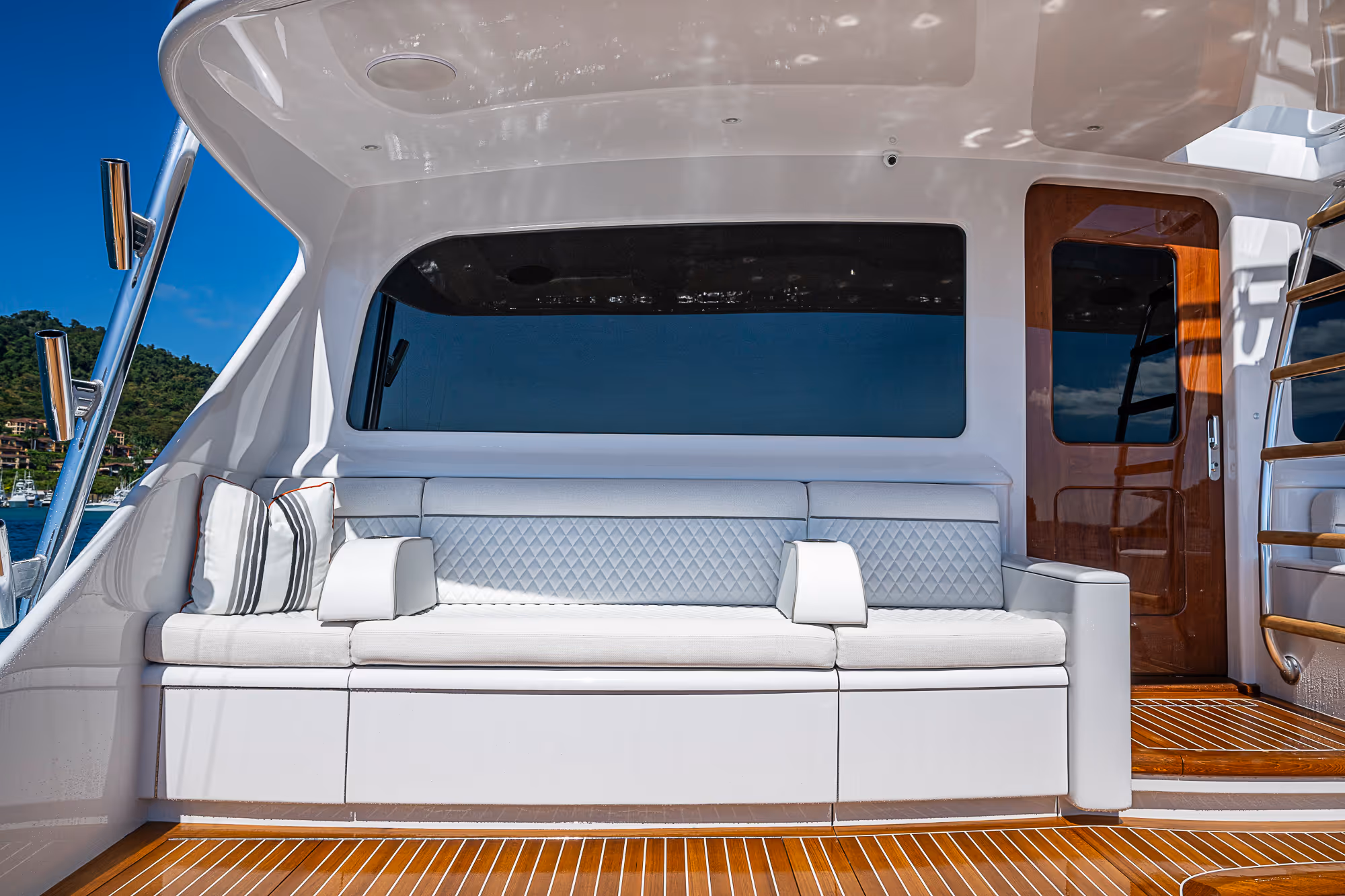 White cushioned seating area on a yacht with wooden deck and a wooden door to the right under a white canopy.
