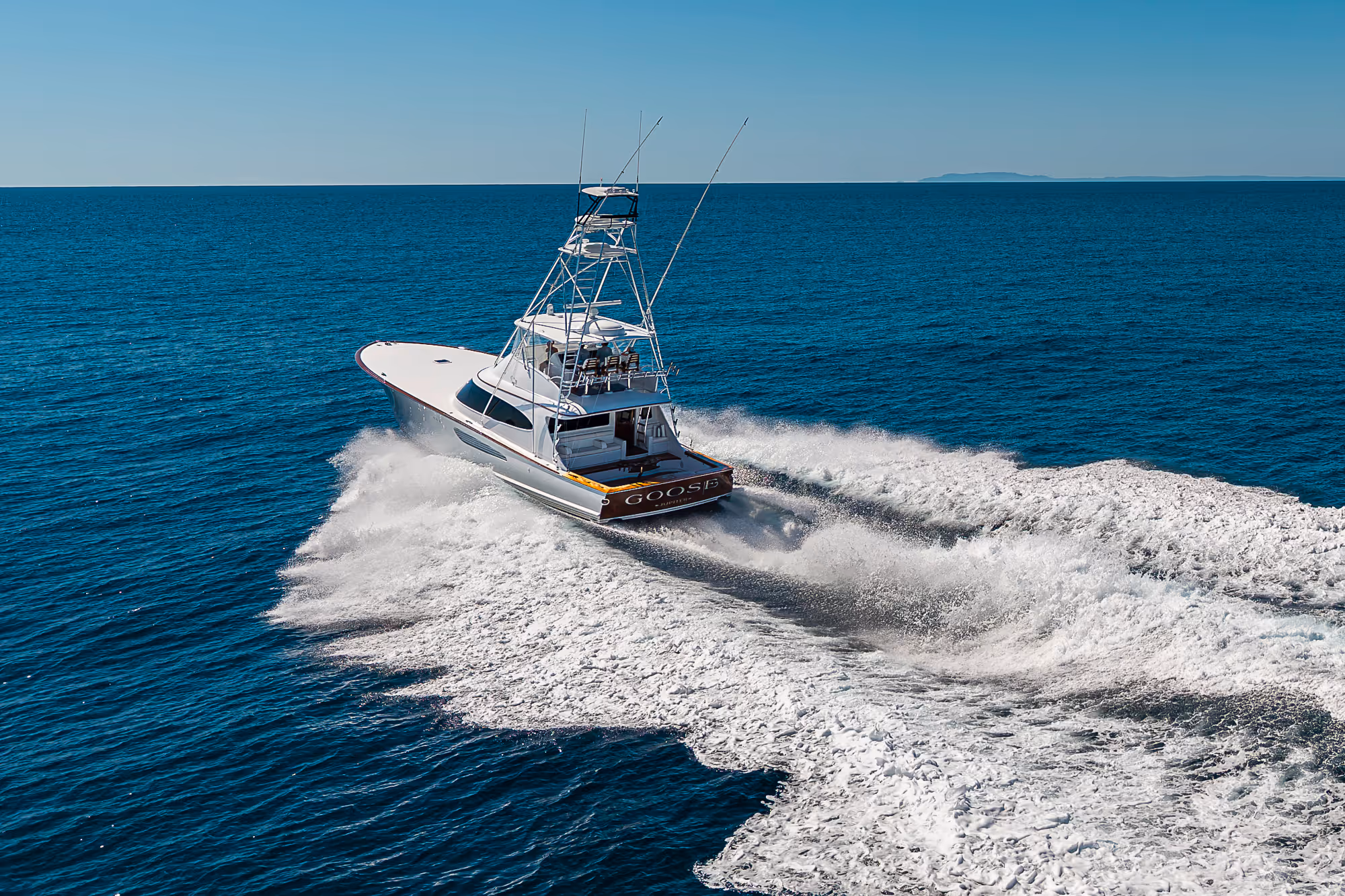 Fishing boat named Goose speeding through blue ocean water leaving a frothy white wake behind.