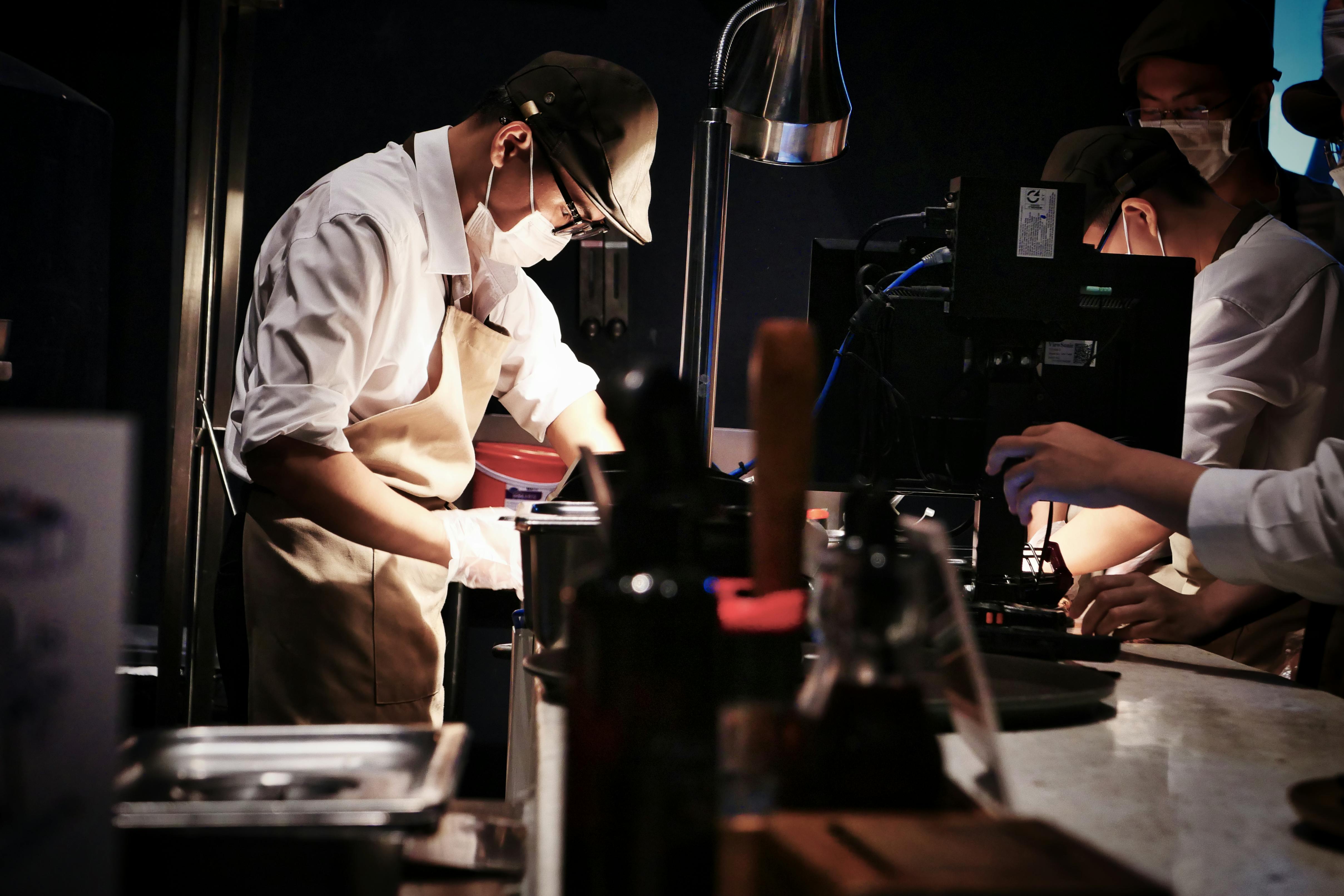 QSR kitchen team working under pressure at a service pass — the franchise compliance paradox between documented brand standards and operational reality at 9pm on a Saturday