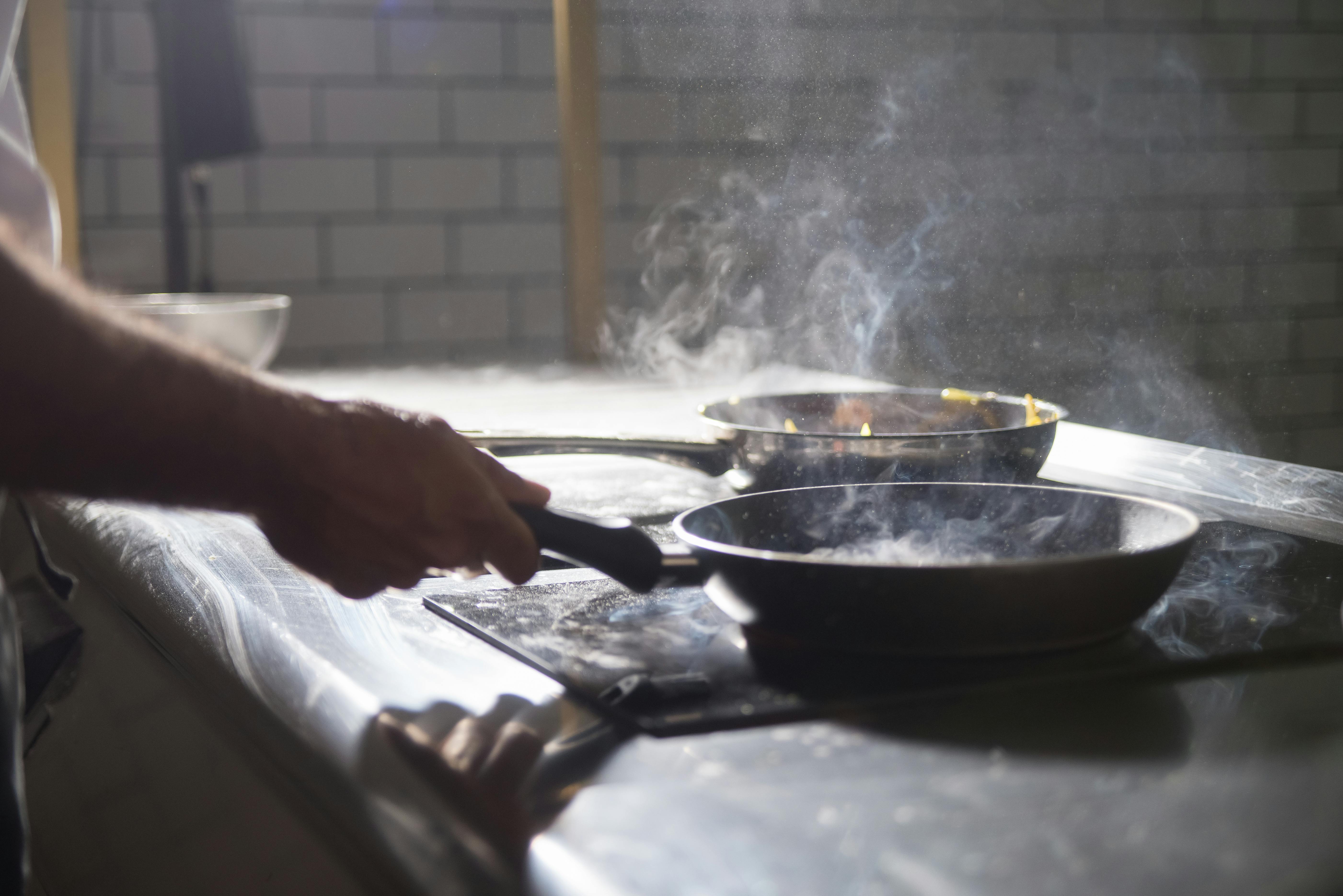 Close-up of a kitchen worker wearing blue food safety gloves slicing cooked meat on a black cutting board, showcasing safe preparation practices to minimize temperature-control risks.