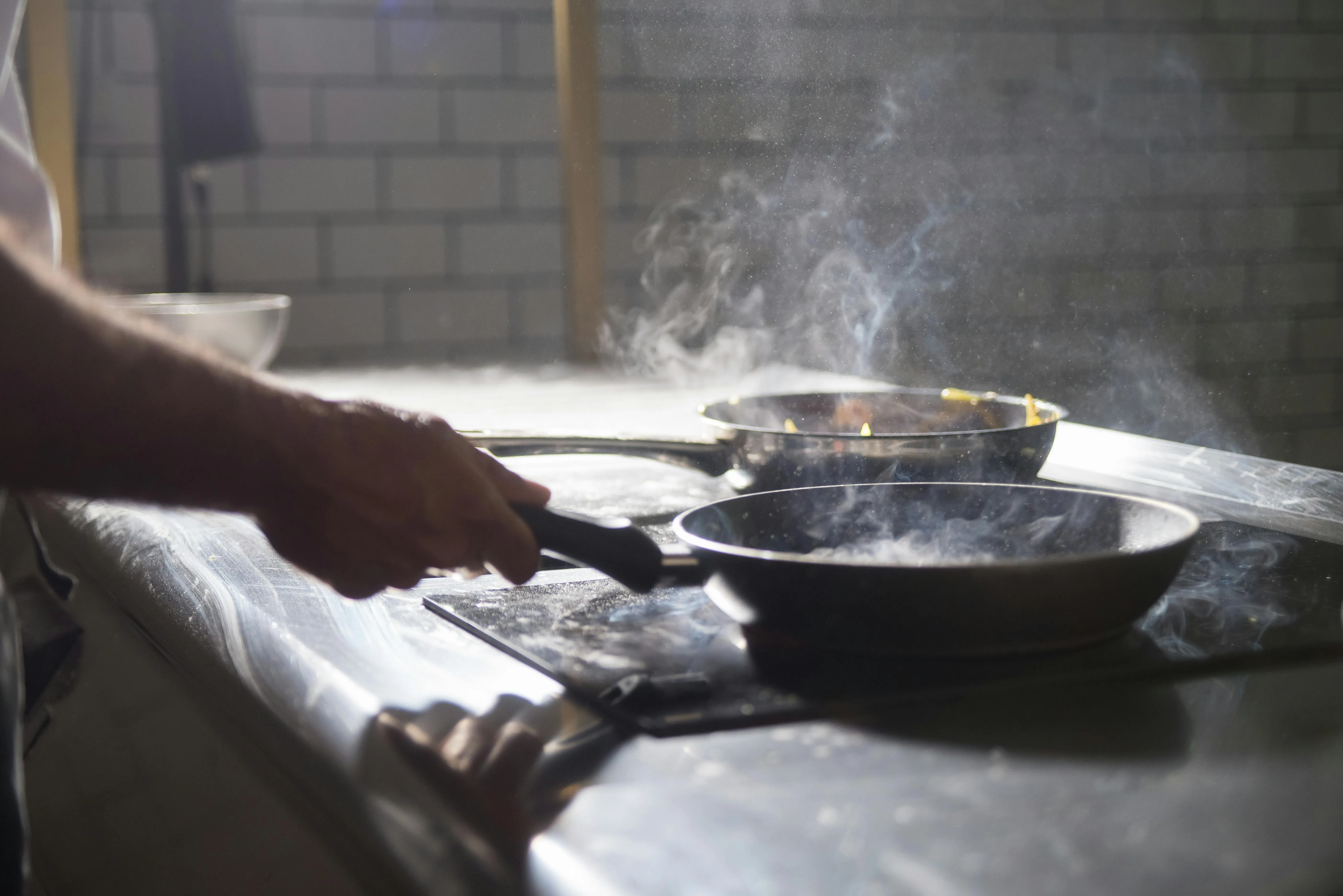 Close-up of a kitchen worker wearing blue food safety gloves slicing cooked meat on a black cutting board, showcasing safe preparation practices to minimize temperature-control risks.