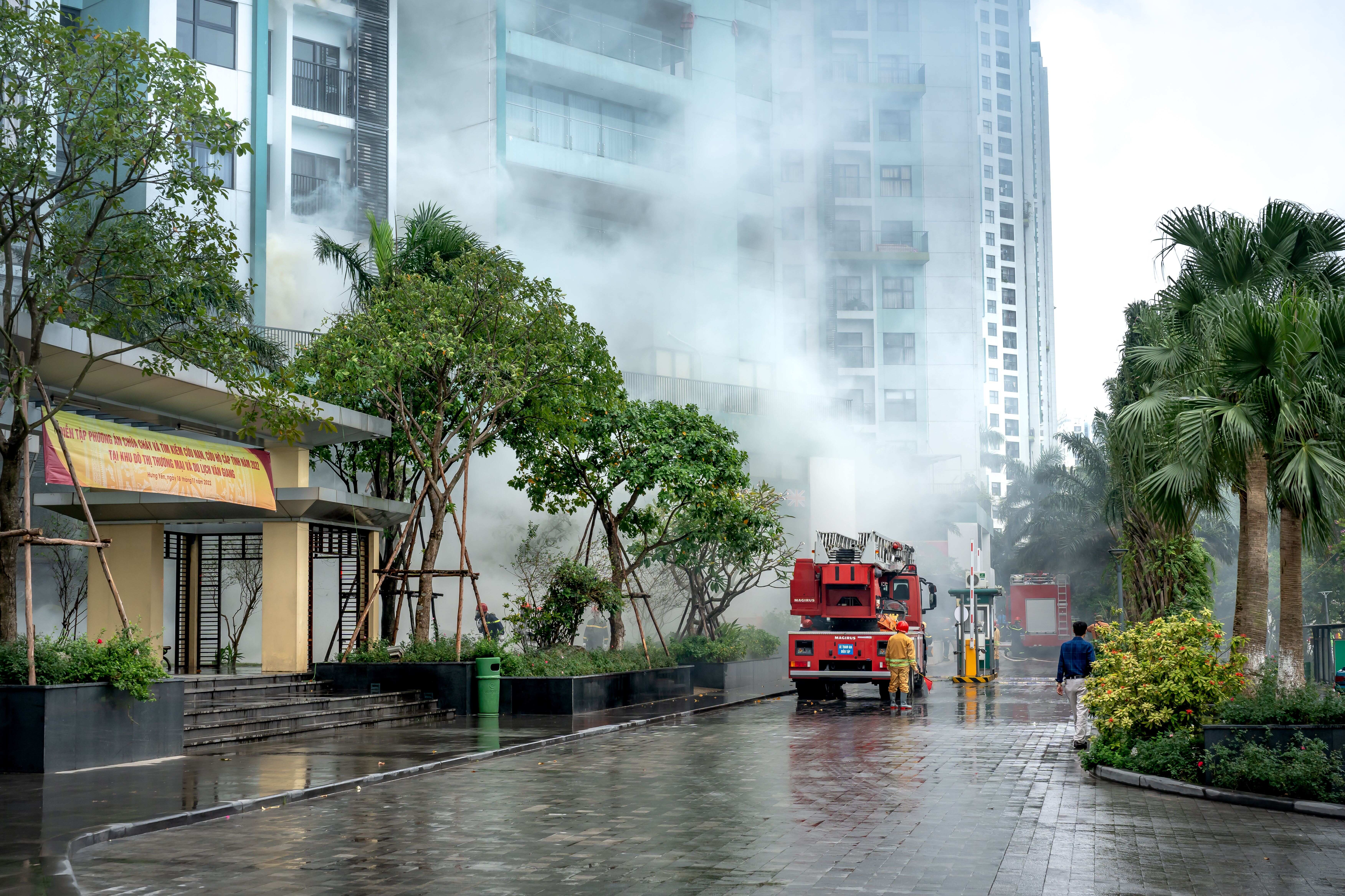 Fire truck parked outside a modern residential building surrounded by dense white smoke during an emergency response.