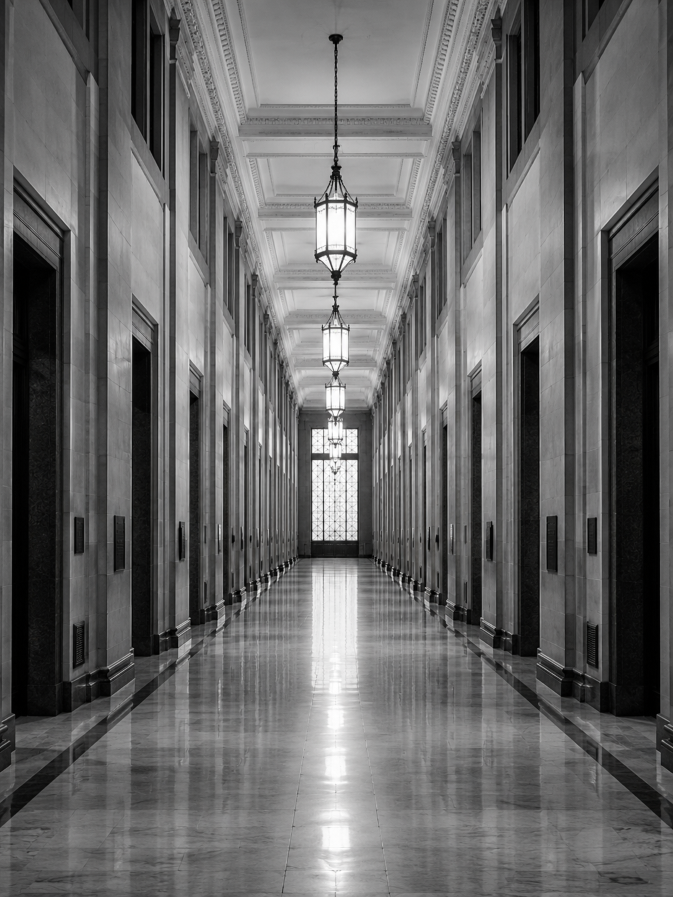 Long narrow marble hallway with tall ceilings and hanging lantern lights in grayscale.