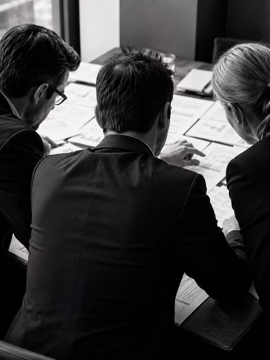 Three business professionals reviewing and discussing documents with charts on a table in an office.