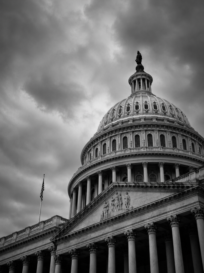 Black and white photo of the U.S. Capitol dome with cloudy sky background.