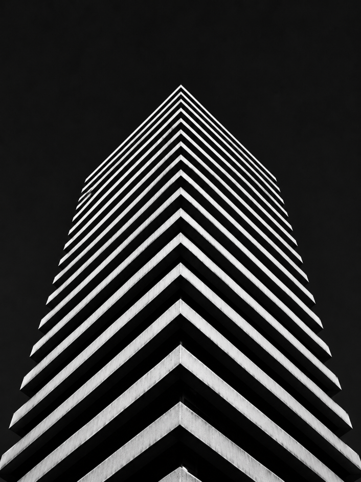 Black and white photo of a tall building corner with repeating horizontal ledges against dark sky.