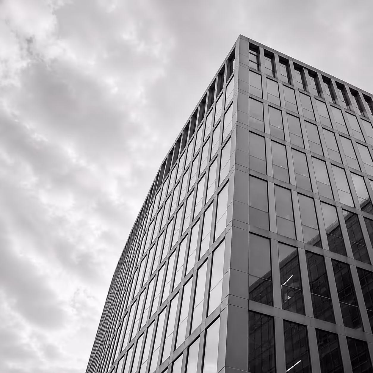 Modern office building with reflective glass windows under a cloudy sky.
