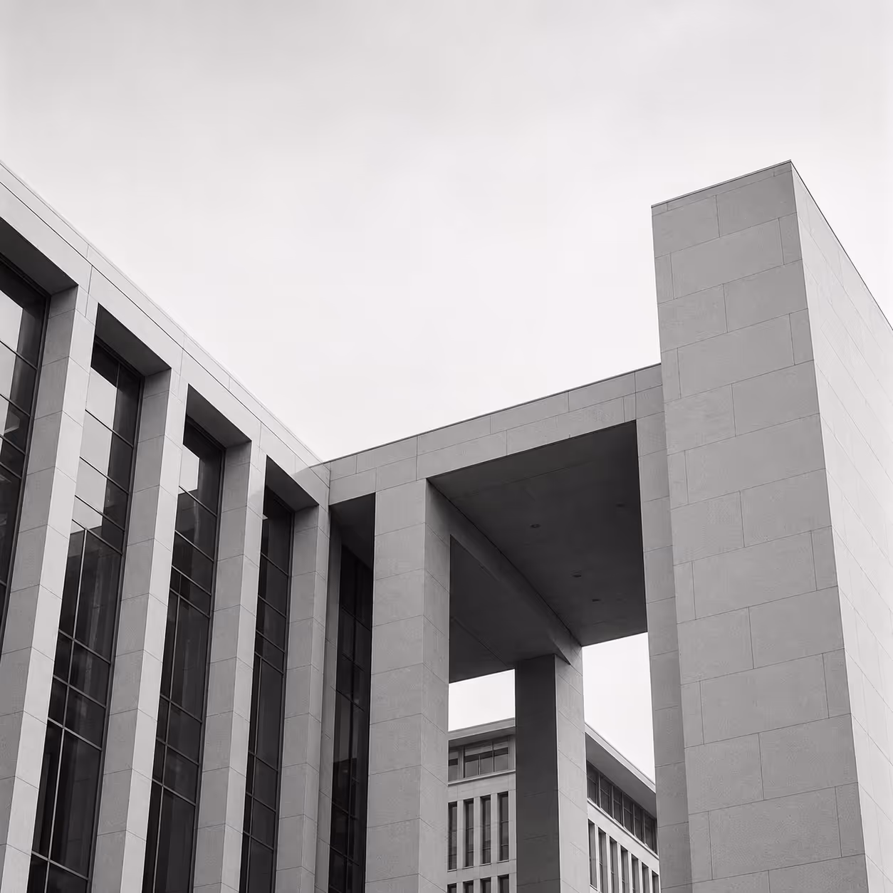 Modern office building with tall vertical windows and large square columns in grayscale.