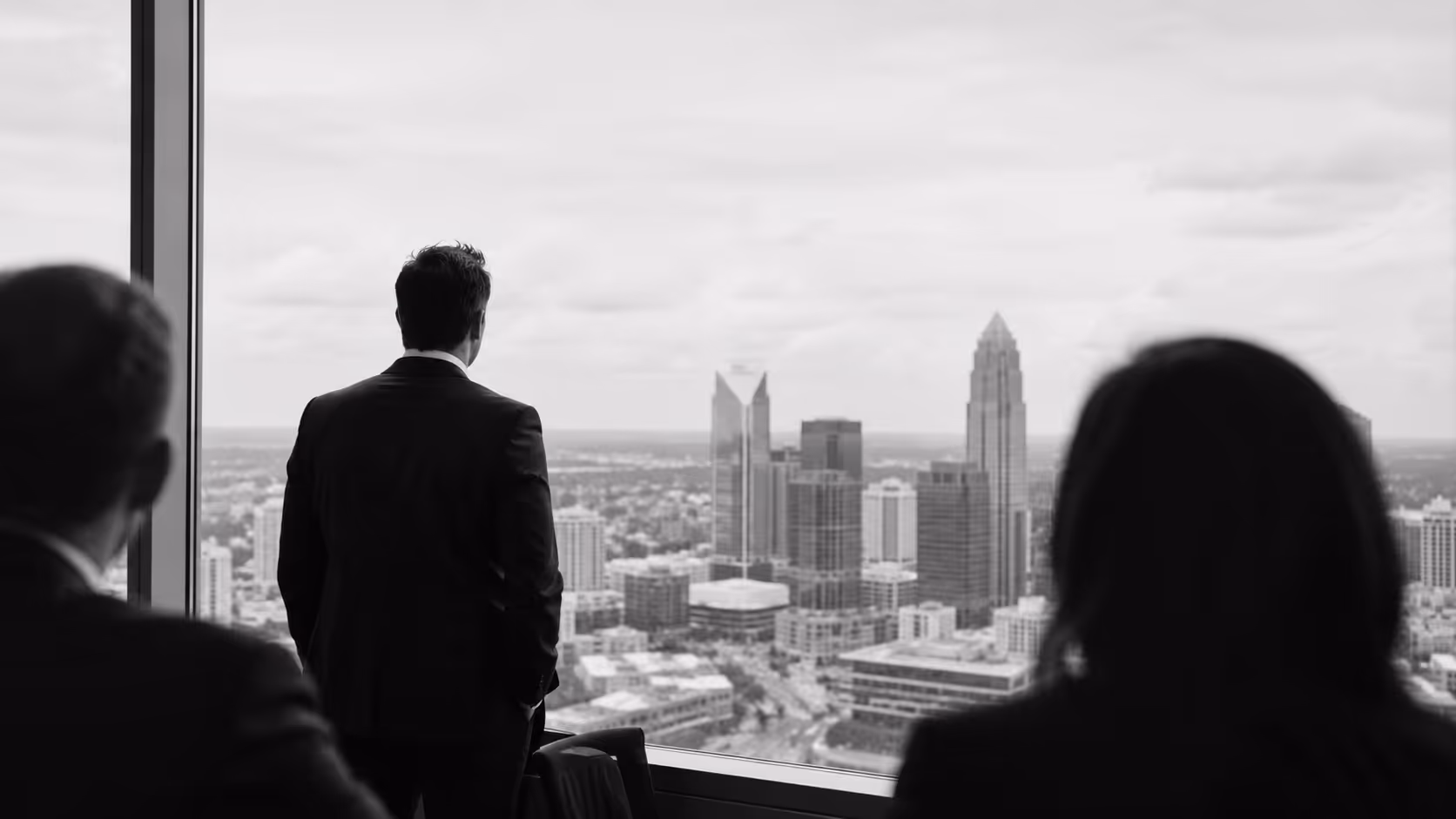 Three businesspeople in suits looking out a large window at a city skyline in black and white.