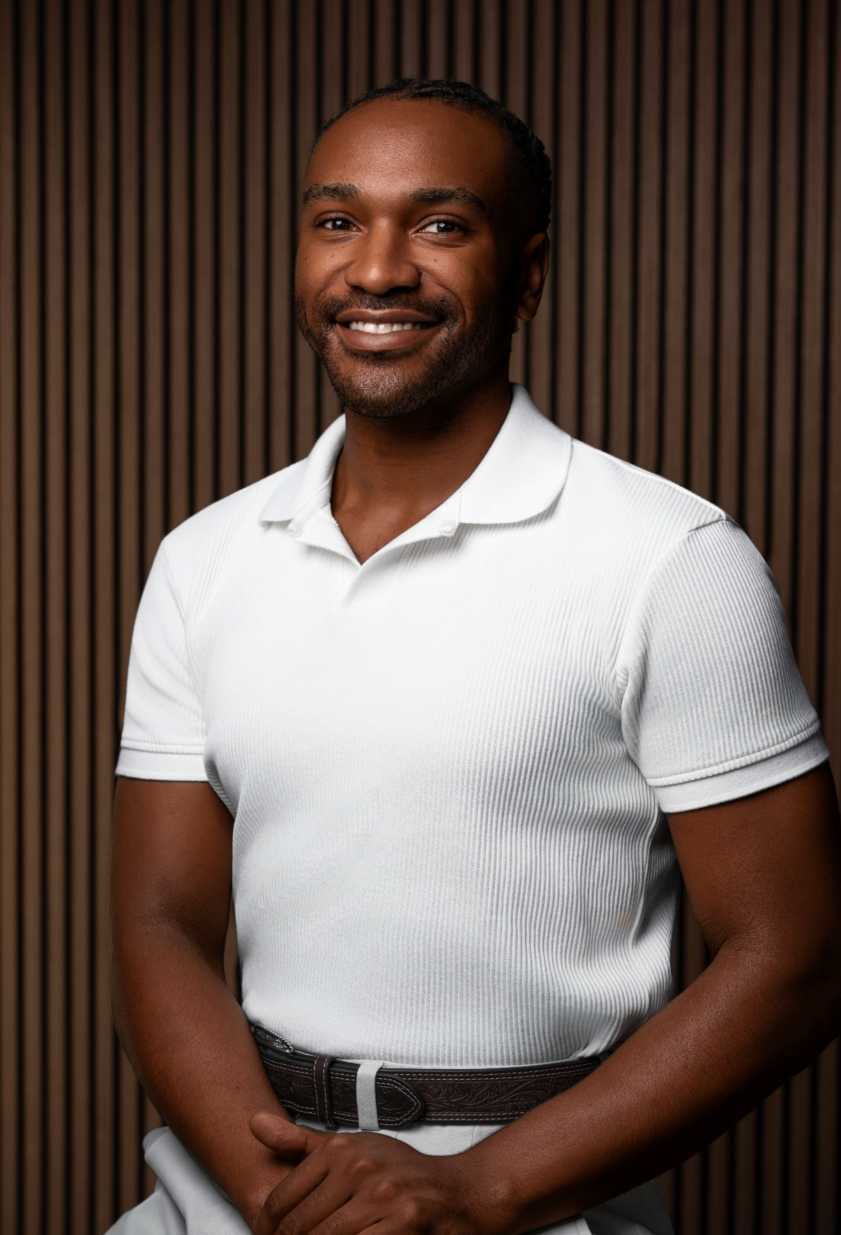 Smiling man with short curly hair wearing a gray zip-up sweater with a red embroidered logo.