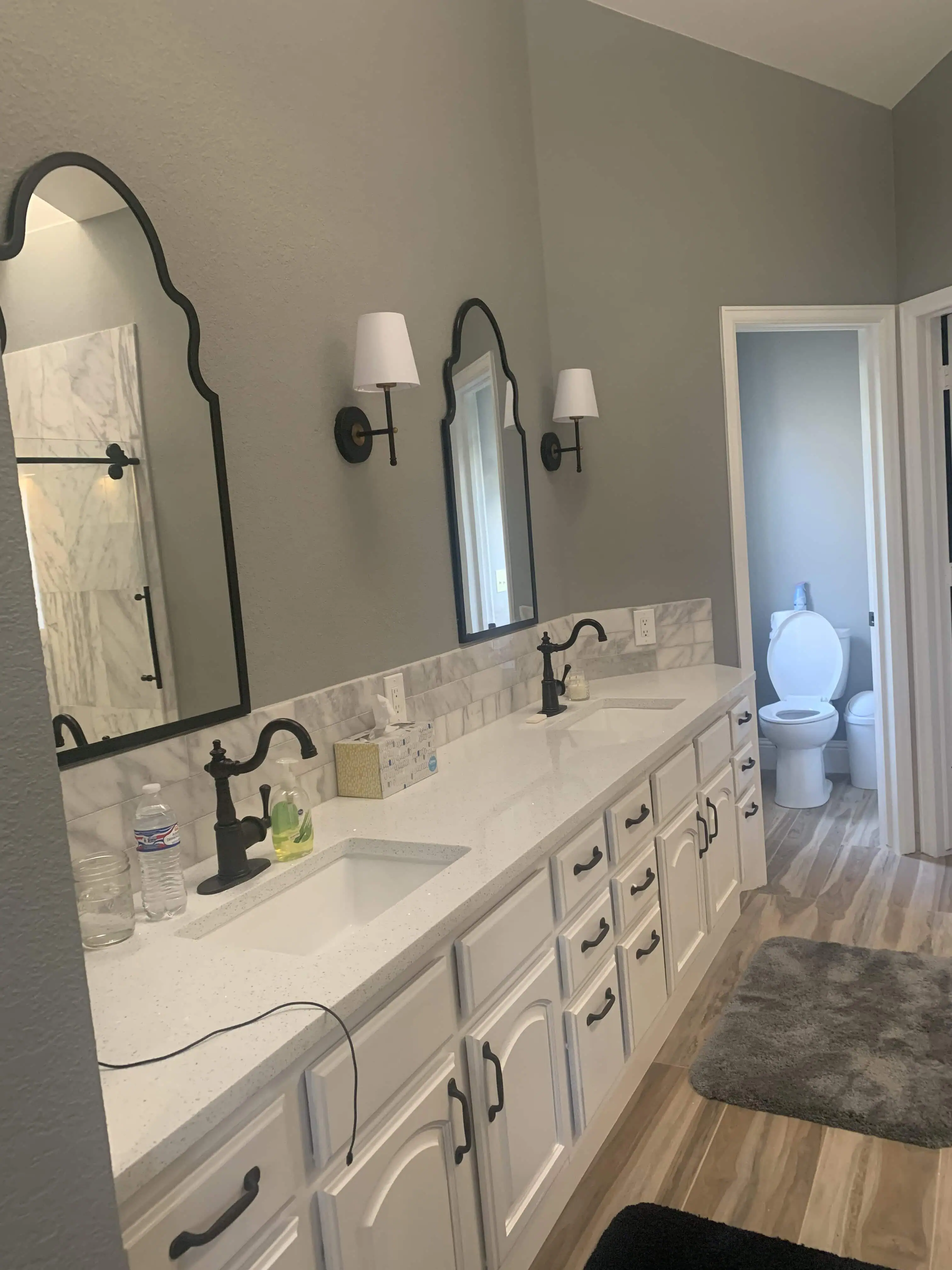 Modern bathroom renovation by Blue Mountain Remodeling in Denver. Features a double sink vanity with white cabinets, marble countertops, decorative mirrors, and contemporary lighting fixtures.