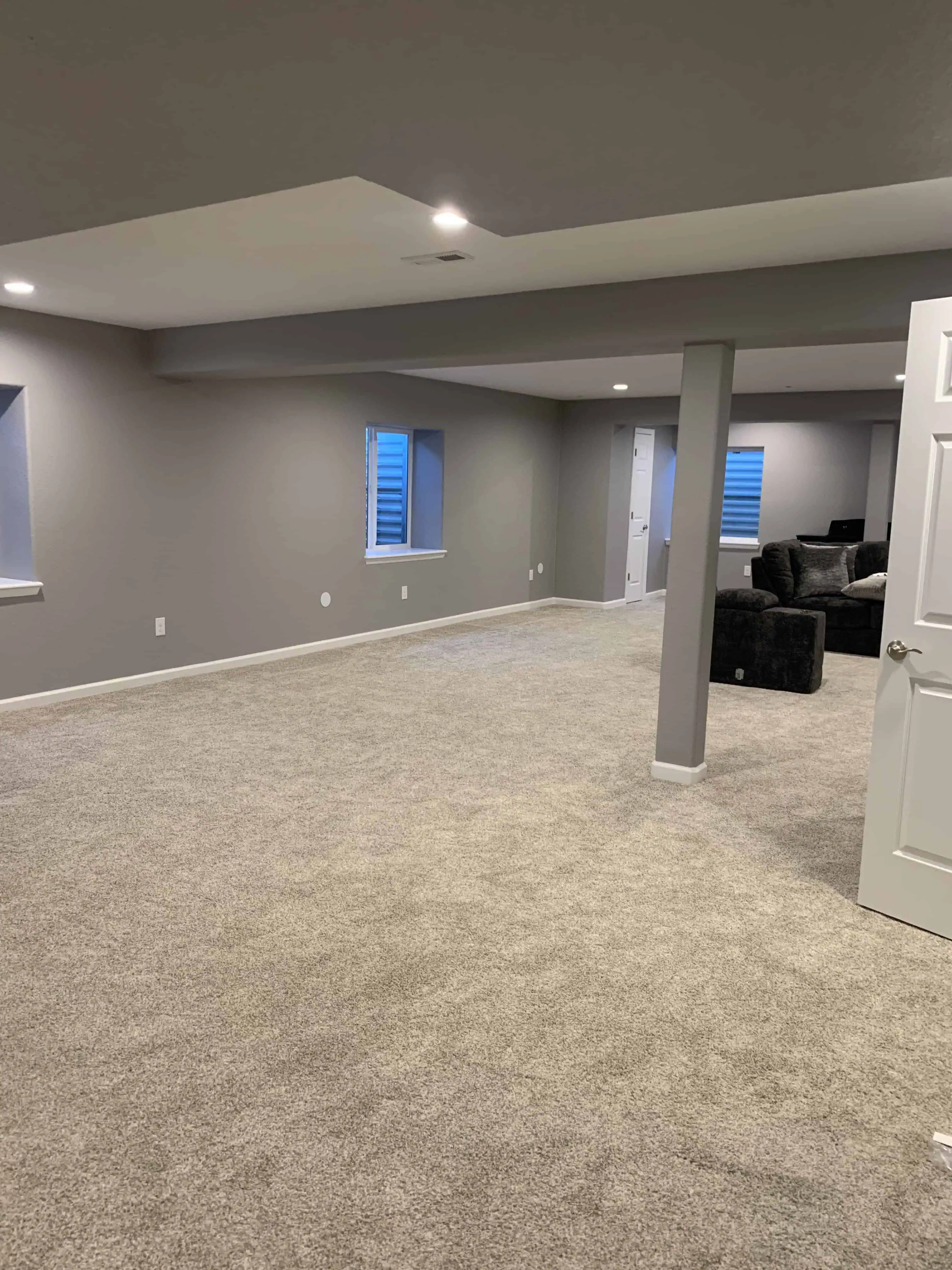 Spacious newly remodeled basement area with gray walls, plush carpet flooring, and modern recessed lighting in a Denver home renovation by Blue Mountain Remodeling.