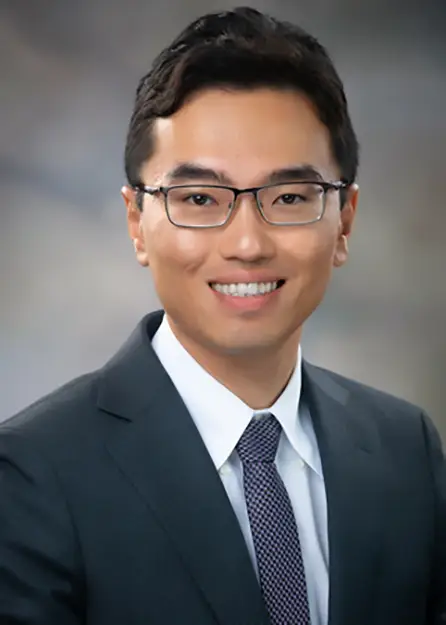 Dr. Anqi Luo smiling at the camera in a dark blue suit and tie.