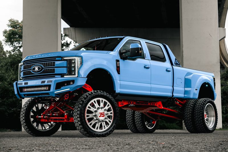 Lifted blue Ford F-350 dually showing red AnyLevel suspension under a bridge