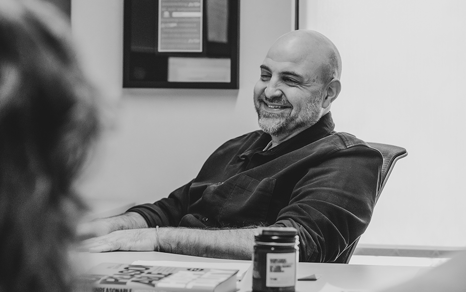 Man smiling and talking to a coworker while sitting at a desk in an office.