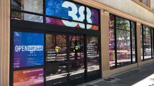 Modern storefront with large black-framed glass windows and doors displaying Open San Jose branding and community-oriented text.