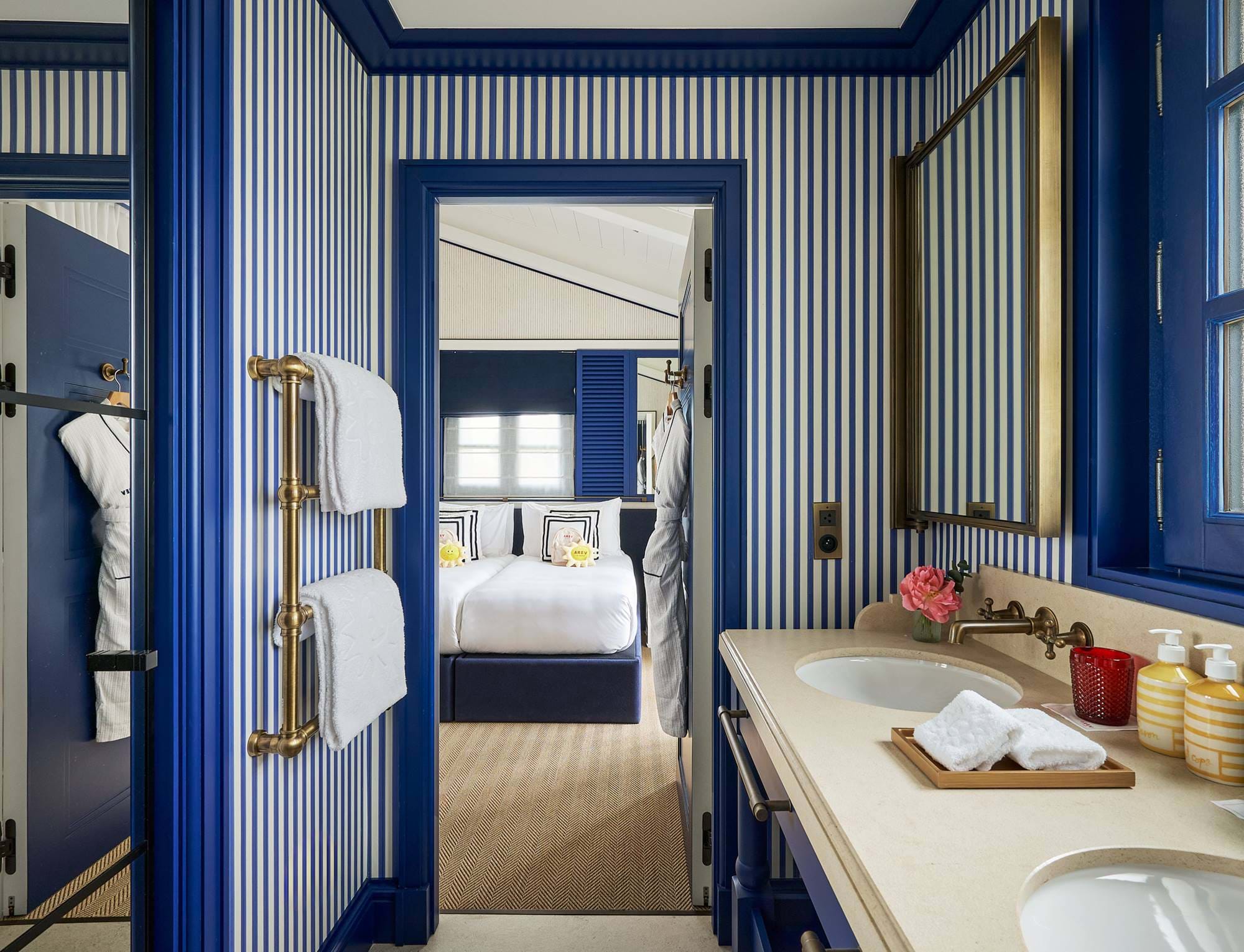 Elegantes Badezimmer im AREV Hotel in Saint-Tropez mit leuchtend blauen Zierelementen, einem Doppelwaschtisch und Blick ins Schlafzimmer.