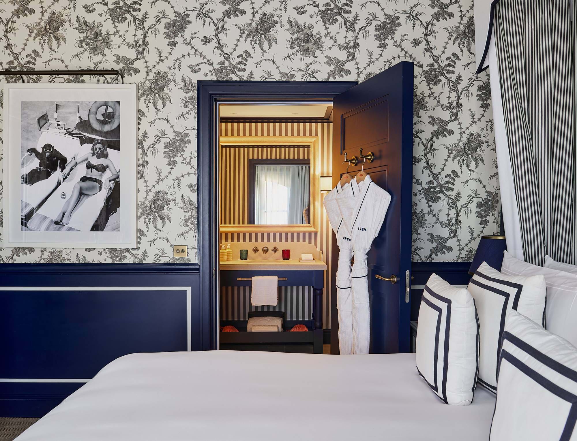 Blick vom Schlafzimmer auf das private Badezimmer im Hotel AREV in Saint-Tropez, das mit blauen Holzarbeiten und floralen Mustern verziert ist.