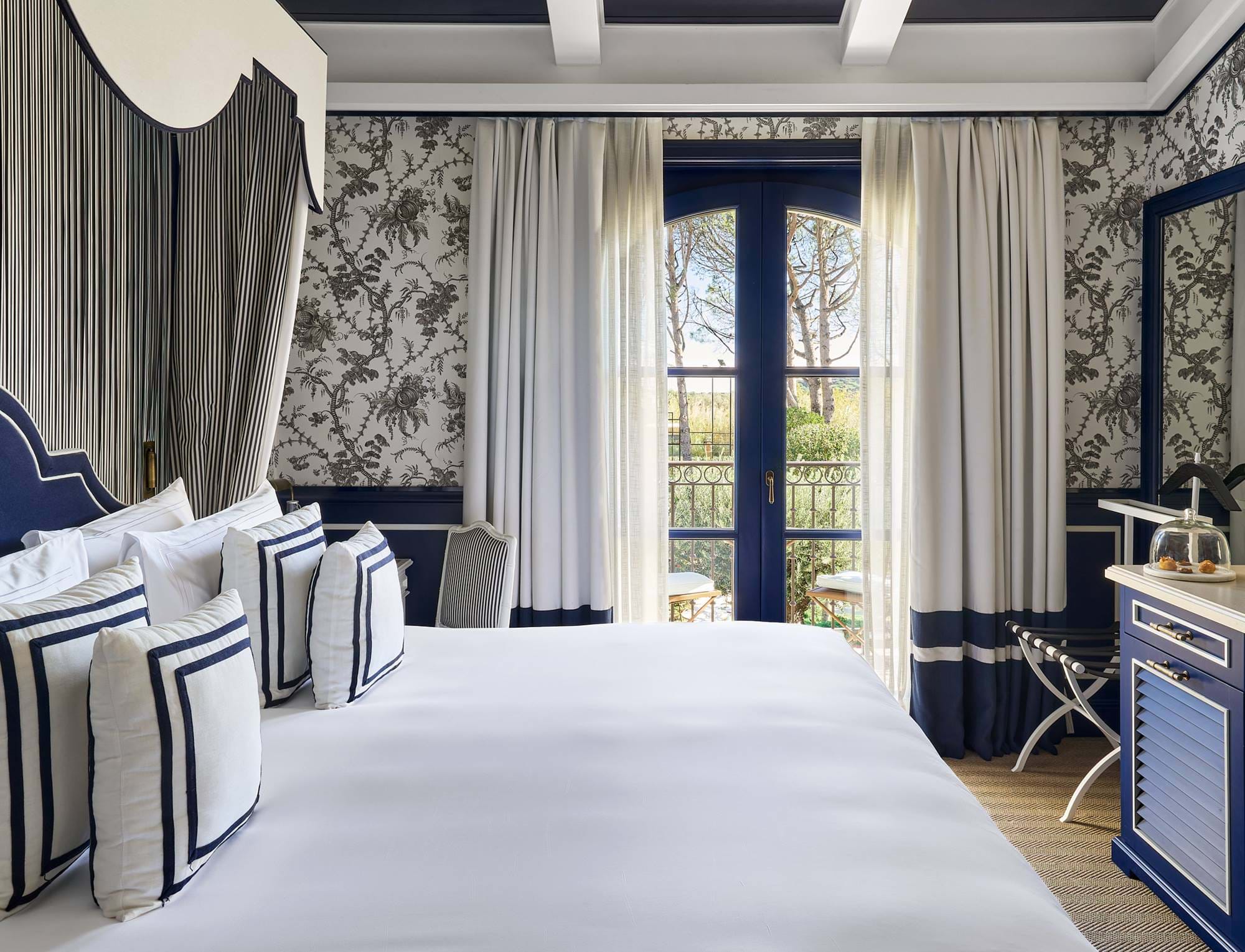 Luxuriöses Schlafzimmer im AREV Hotel in Saint-Tropez mit Kingsize-Bett, eleganter Blumentapete und Gartenblick vom Balkon.