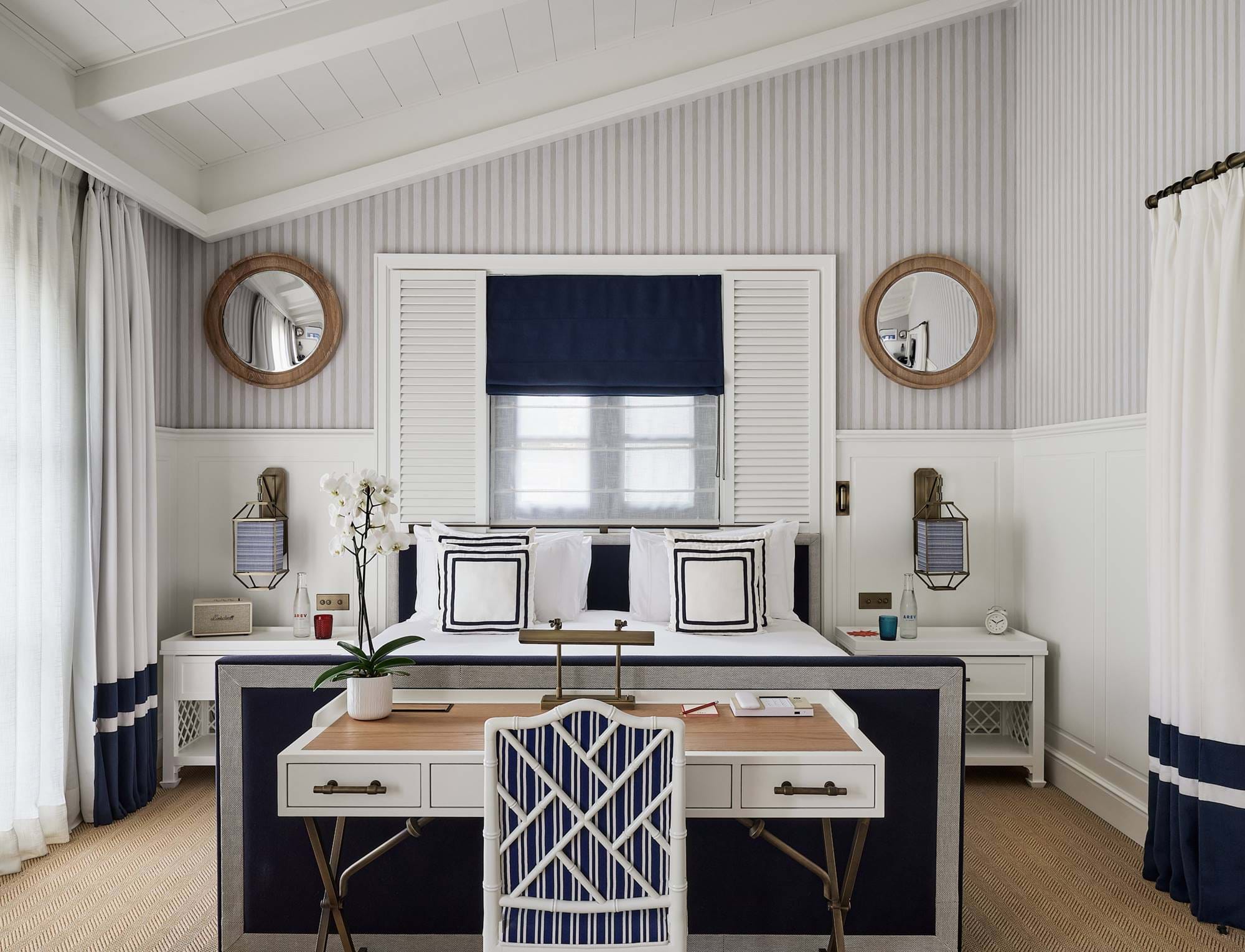 Vorderansicht eines repräsentativen Doppelzimmers im Hotel AREV in Saint-Tropez mit einem Designerschreibtisch, einem Kingsize-Bett und einem symmetrischen weißen Kopfteil.