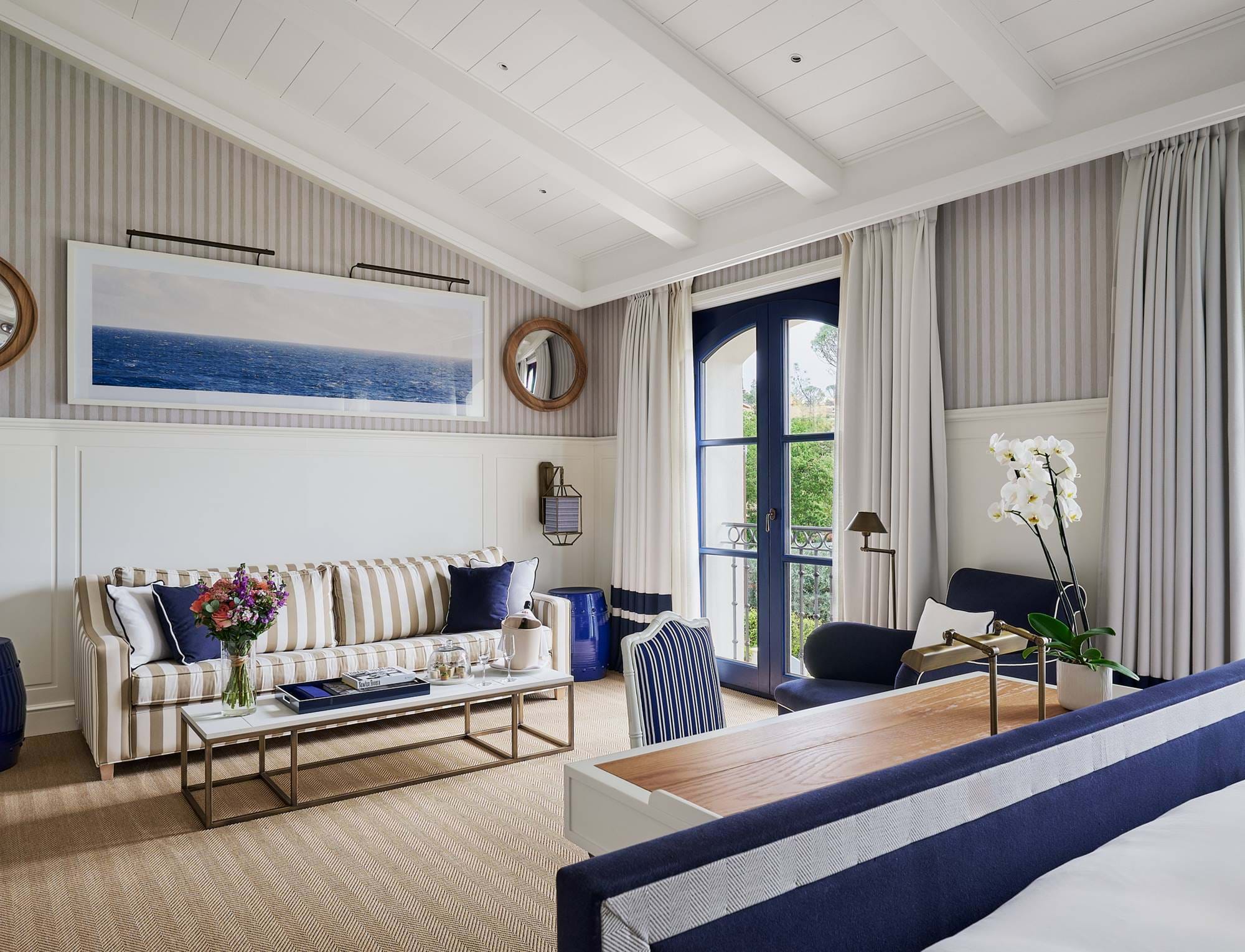 Eleganter Wohnbereich der Suite im AREV Hotel in Saint-Tropez mit gestreiftem Sofa, modernem Couchtisch und großem blauen abstrakten Kunstwerk.