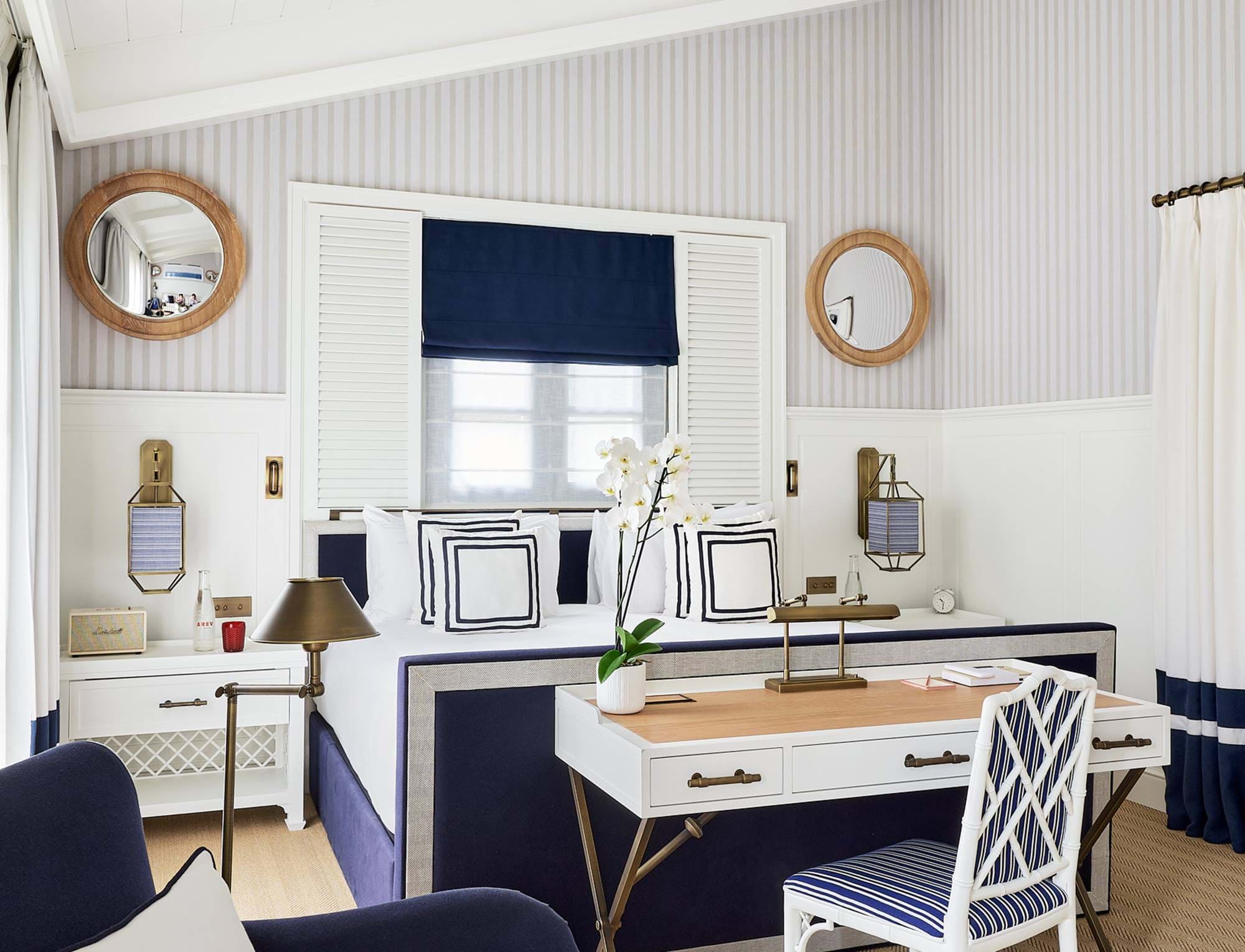 Área de trabalho elegante em um quarto do hotel AREV em Saint-Tropez, com mobiliário branco e azul-marinho, espelhos redondos e decoração refinada.