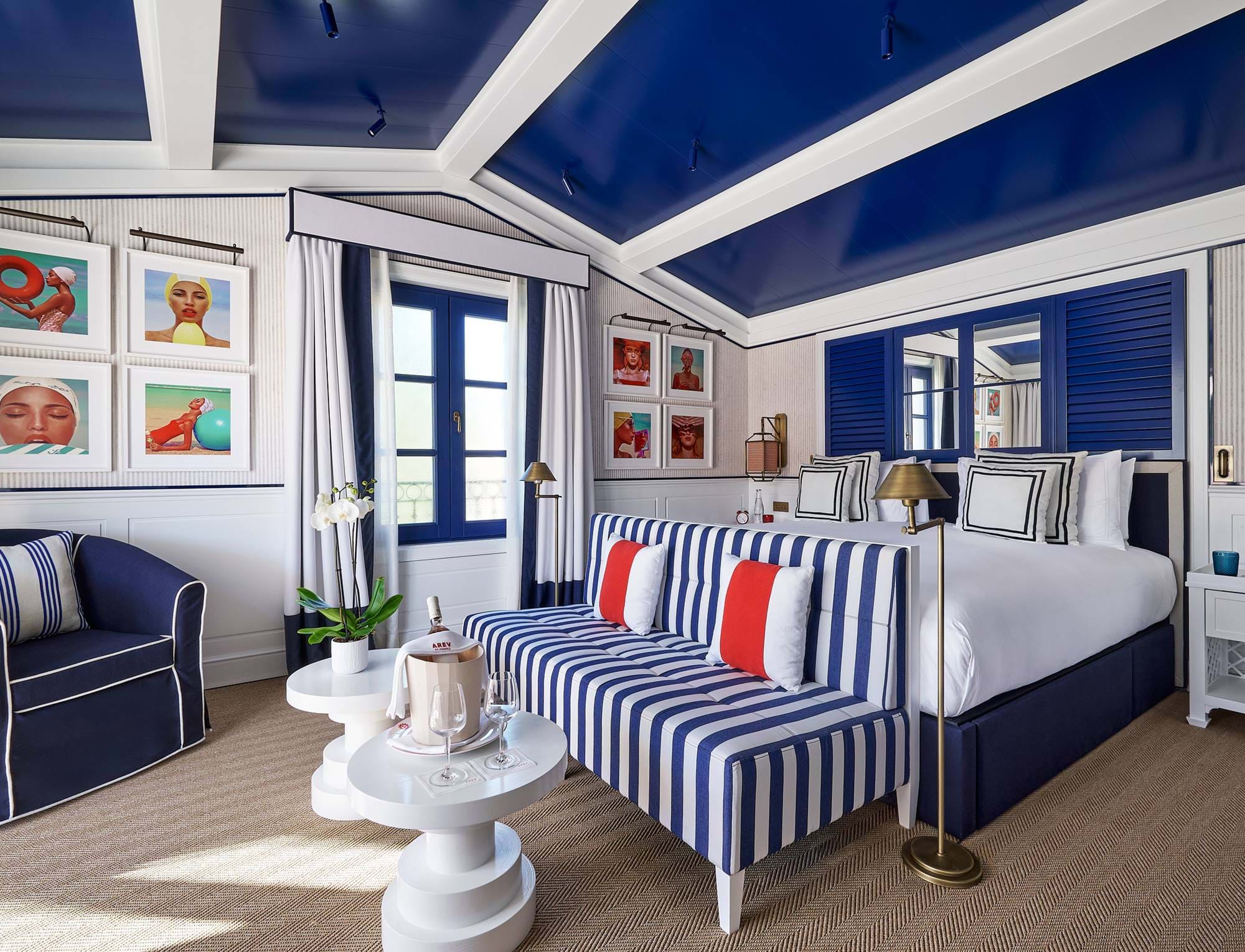 Sitzecke einer repräsentativen Suite im Hotel AREV in Saint-Tropez mit gestreiftem Sofa, blau lackierter Decke und kunstvoller Dekoration.
