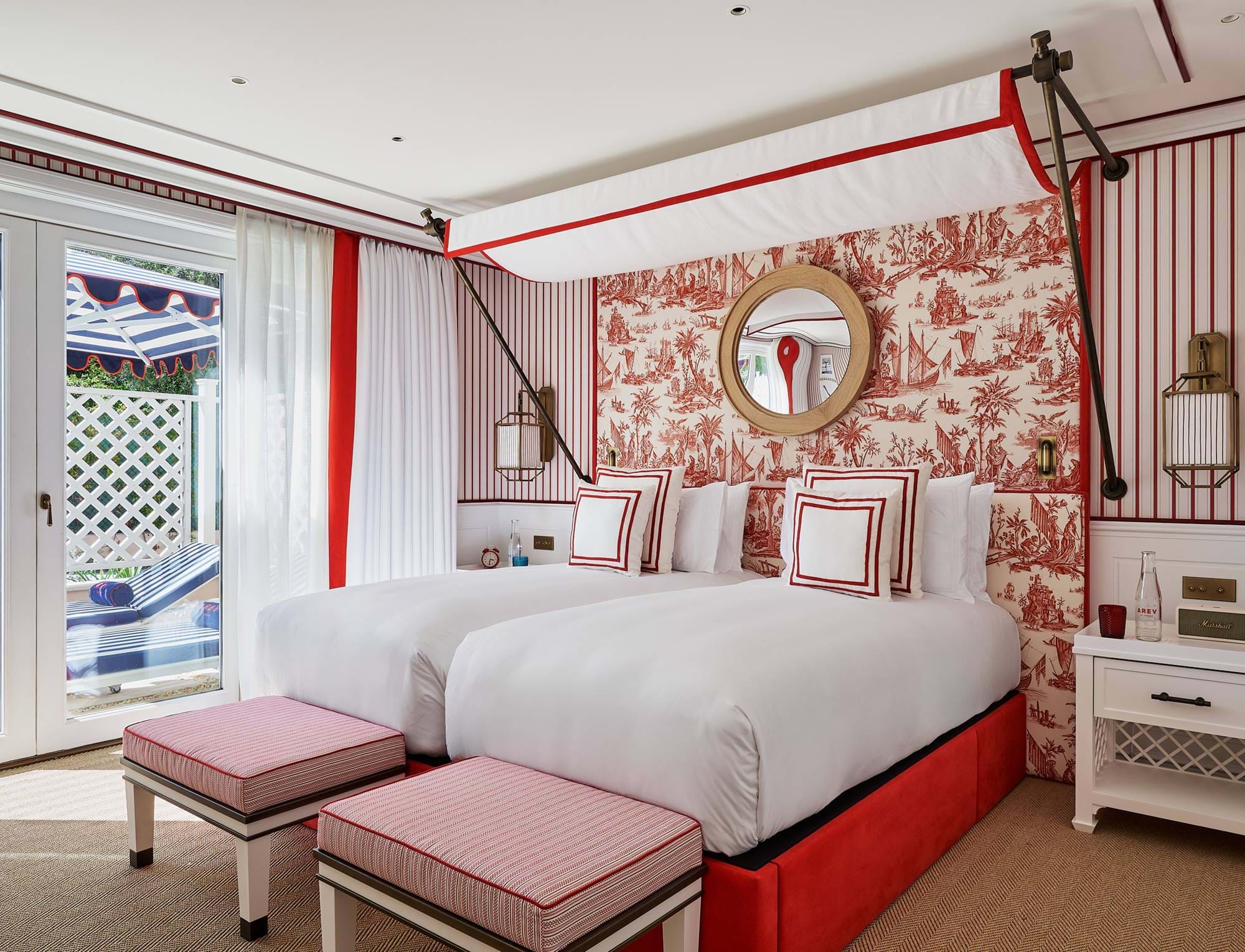 Hochwertiges Gästezimmer im AREV Hotel in Saint-Tropez mit zwei Einzelbetten, rot gemusterter Tapete und sonnigem Balkon.