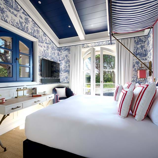 Das helle, luxuriöse Schlafzimmer im AREV Hotel in Saint-Tropez verfügt über ein Kingsize-Bett, ein elegantes blau-weißes Dekor, einen Waschtisch und eine private Terrasse.