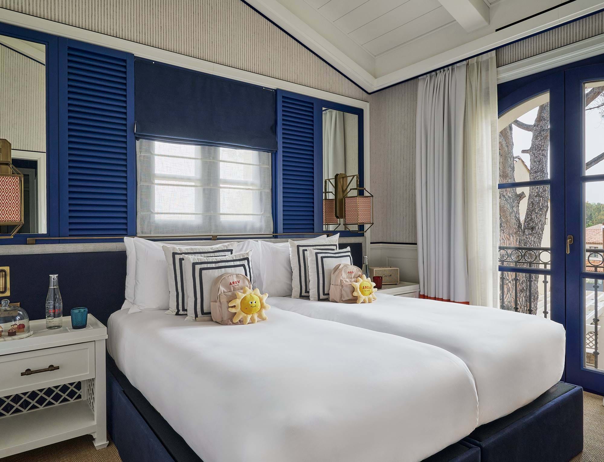 Cama de casal luxuosa com roupas de cama brancas e detalhes em azul no hotel AREV em Saint-Tropez, com vista para uma varanda privativa.