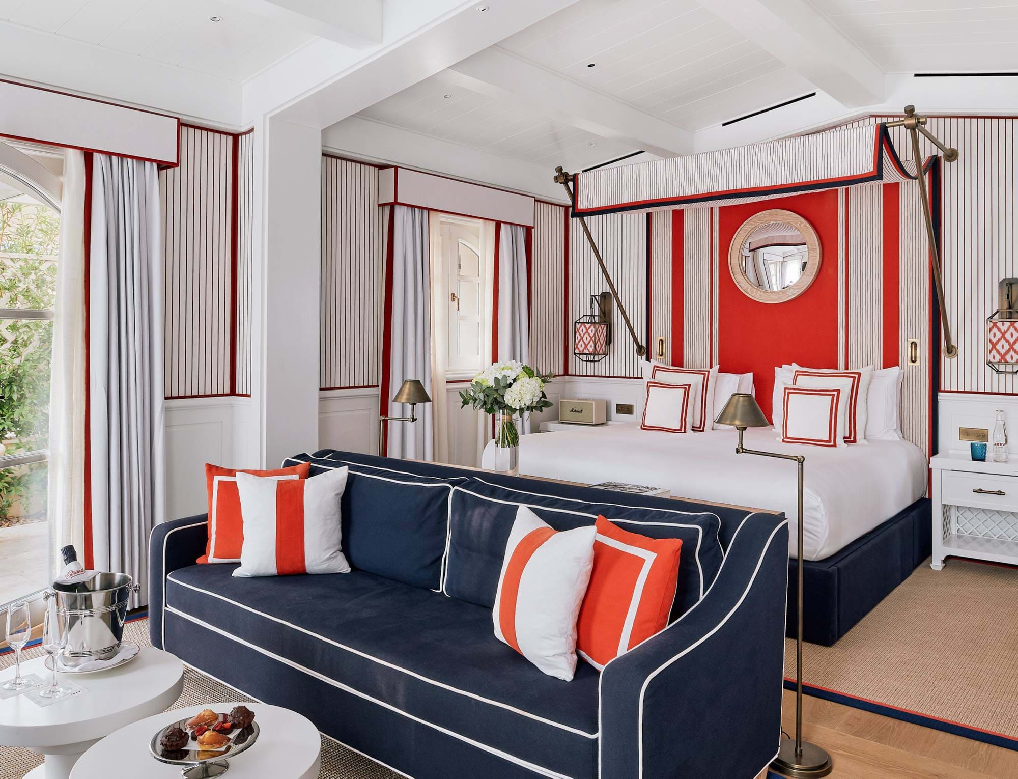Suíte de luxo com cama com dossel, sofá azul-marinho e almofadas listradas no hotel AREV em Saint-Tropez.